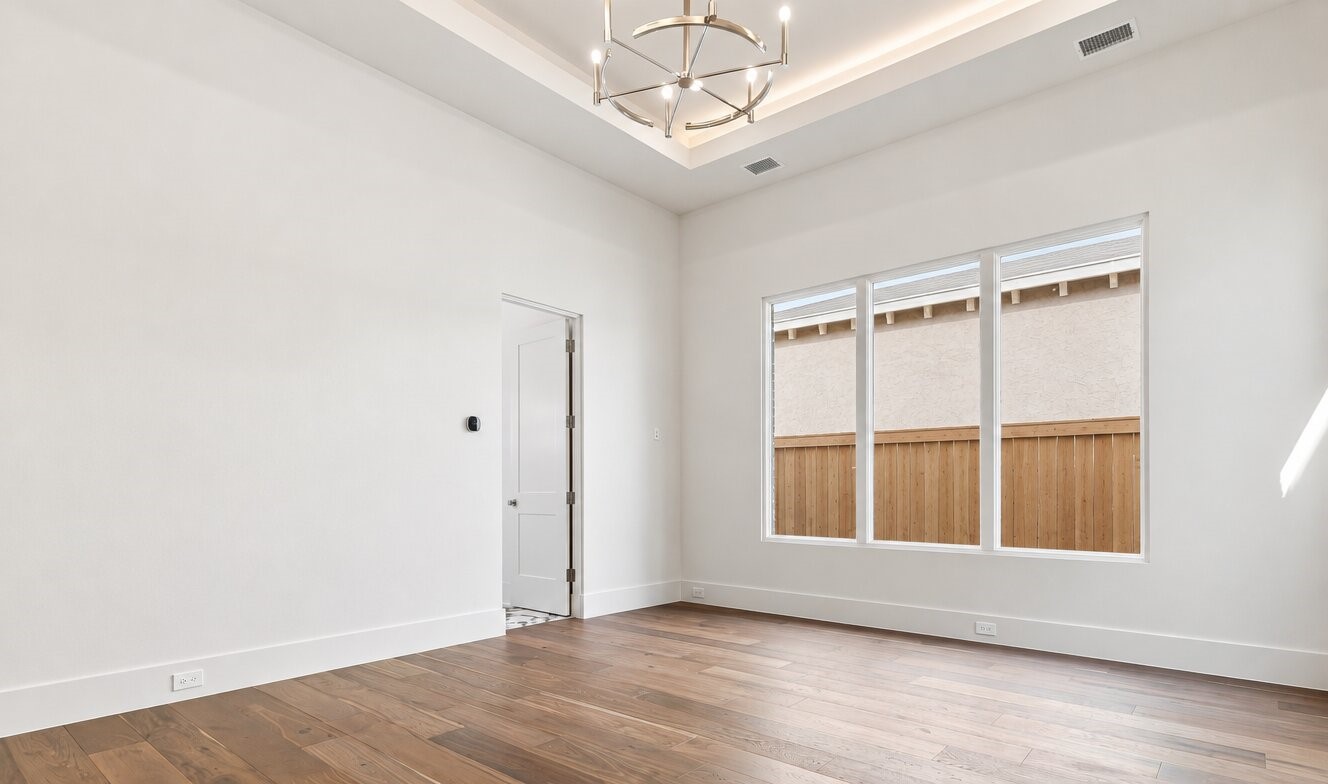 Empty bright room with hardwood floors, a tray ceiling, and three large windows.