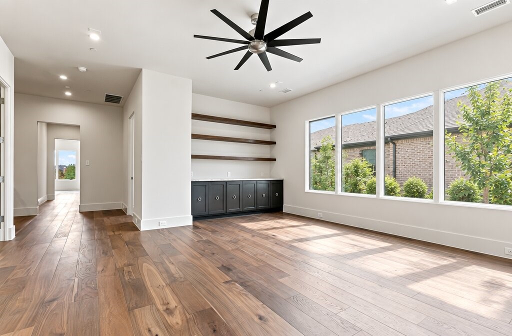Empty living room with wood floors, built-in cabinets and shelves, and large windows.