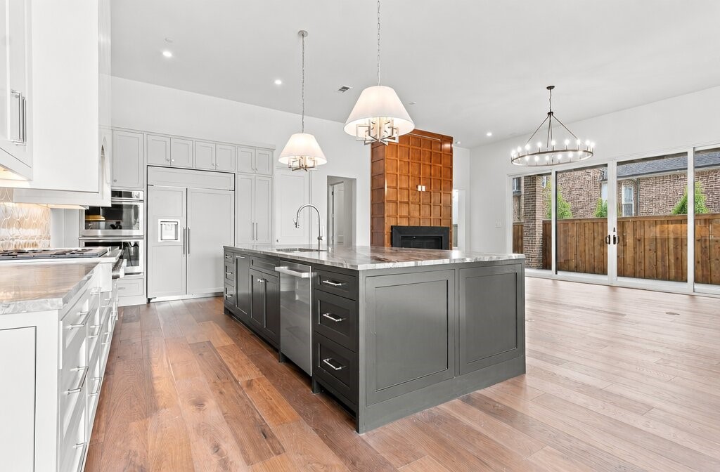 Open kitchen with a large gray island, white cabinetry, wood fireplace wall, and glass doors to a fenced patio.