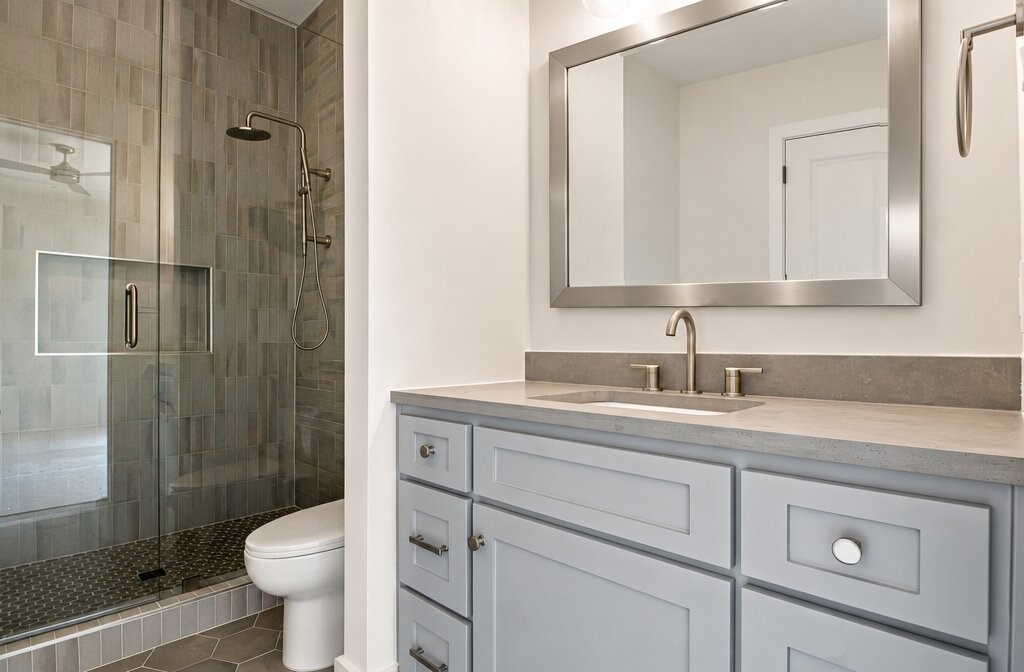 Bathroom with a glass-enclosed gray tile shower and pale blue vanity.
