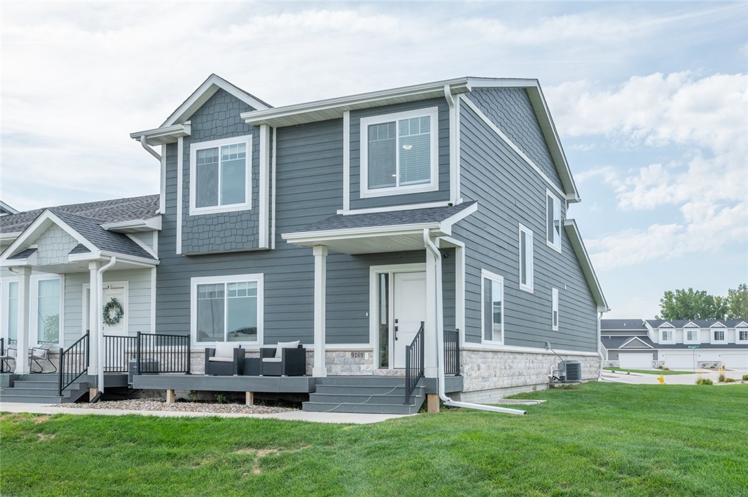 Two-story blue-gray home with white trim, stone foundation, and raised front porch with seating.
