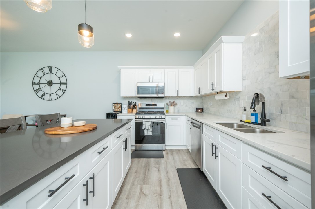 Bright white kitchen with a large gray island, stainless steel appliances, and marble-look backsplash.