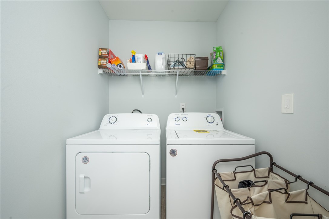 Laundry room with side-by-side washer and dryer, overhead wire shelf, and fabric laundry sorter.