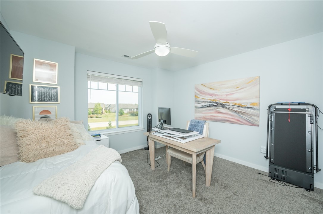 Bedroom with a desk and computer beside the bed, overlooking neighboring homes through a wide window.