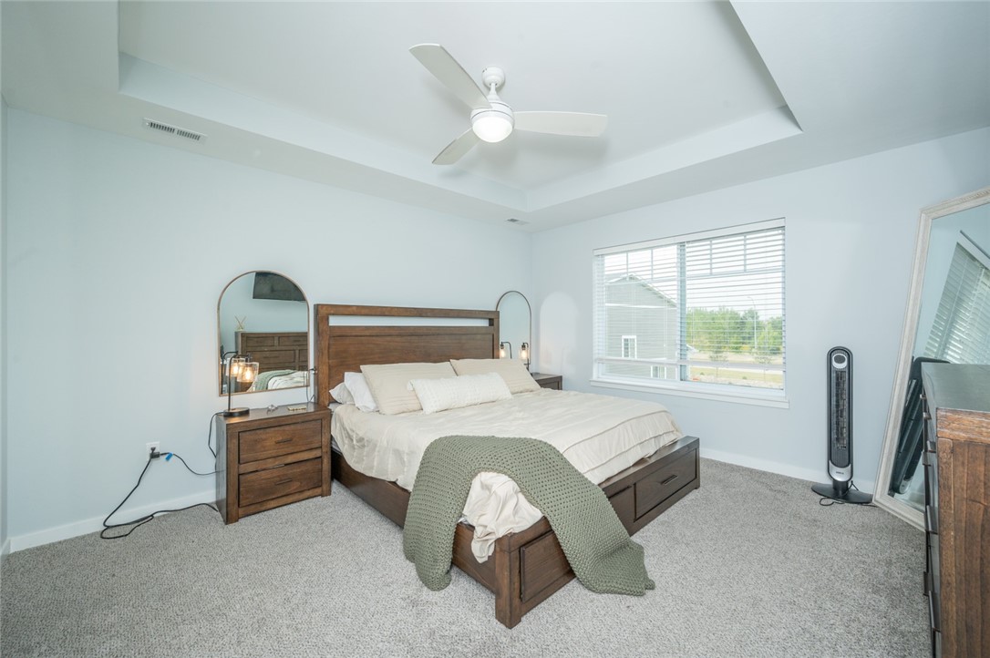 Furnished bedroom with a dark wood bed, green throw, tray ceiling, and large window.