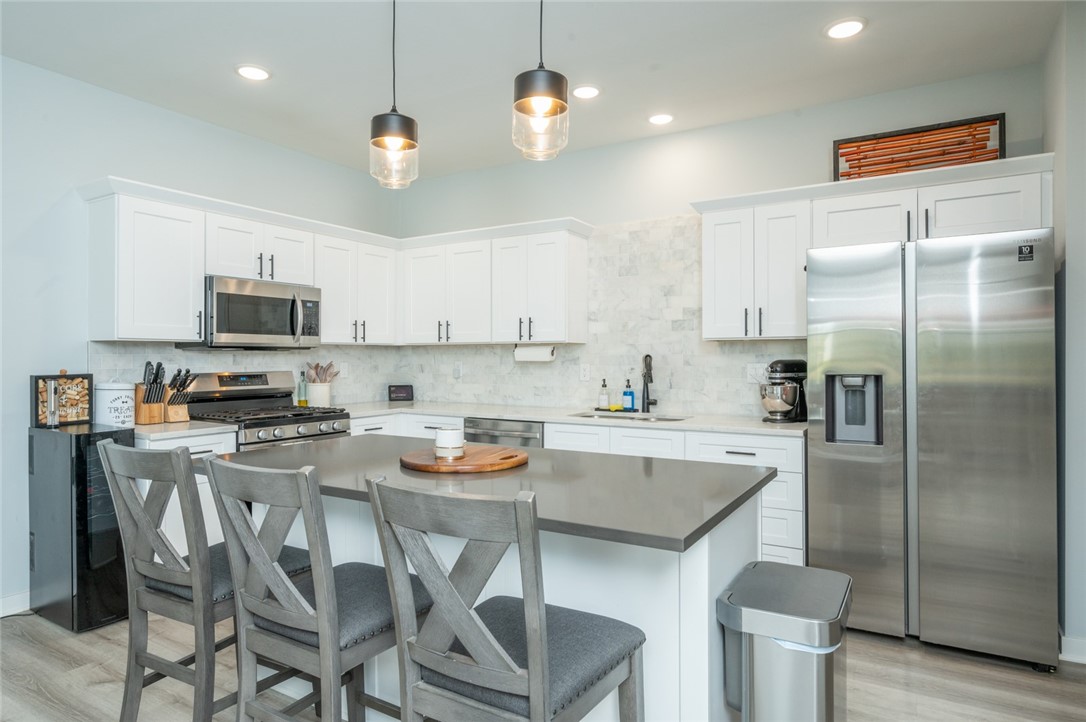 Modern kitchen with white cabinets, stainless steel appliances, and a gray island with three bar stools.