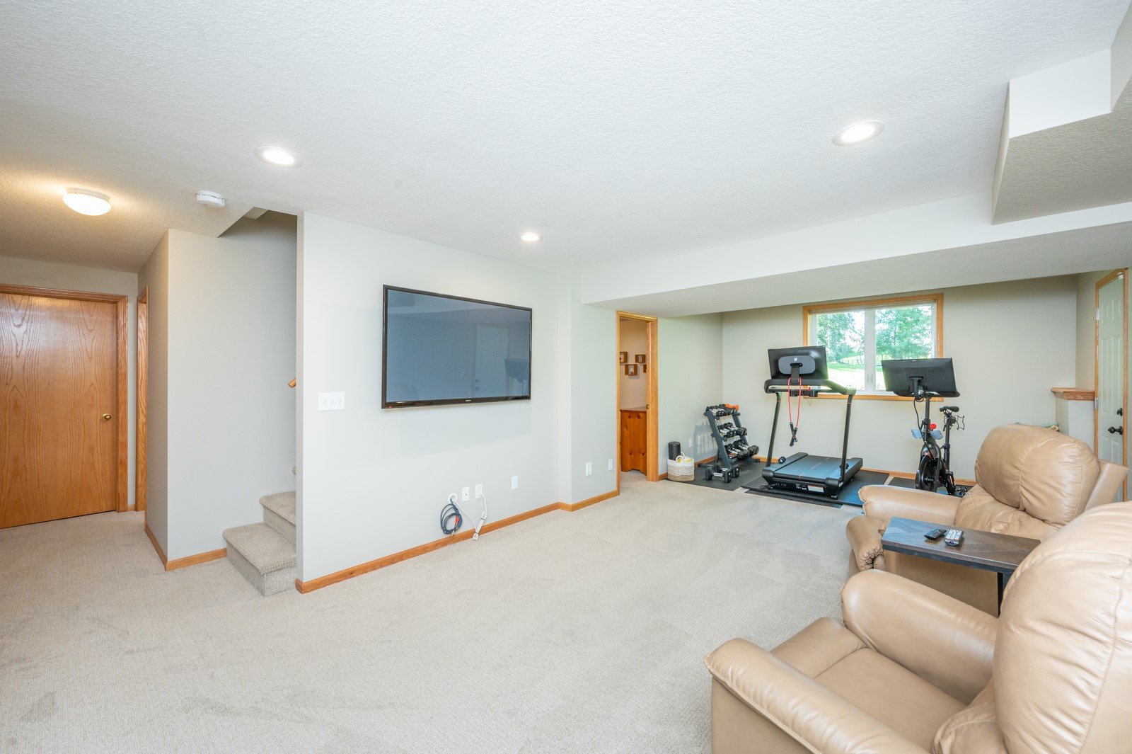 Finished basement recreation room with leather seating and a workout area featuring a treadmill and exercise bike.