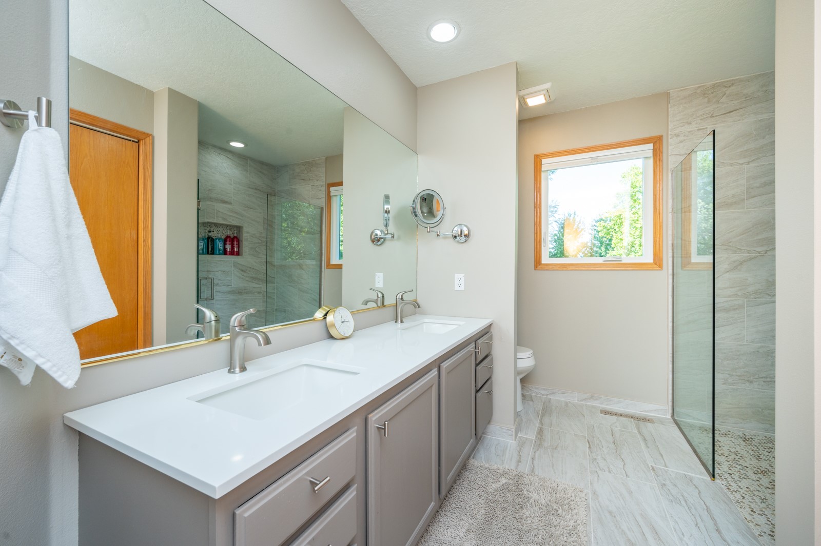 Bathroom with a long double vanity and glass-enclosed, tiled walk-in shower.