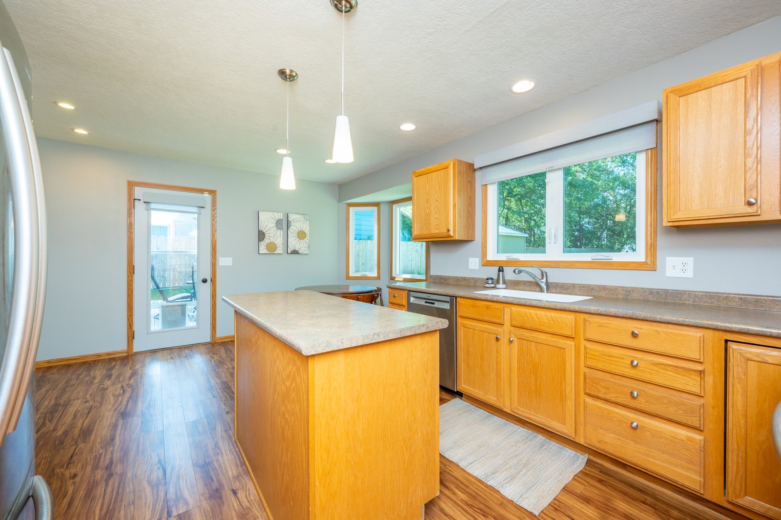Kitchen with honey-colored cabinets, a central island, and a sink beneath a wide window.
