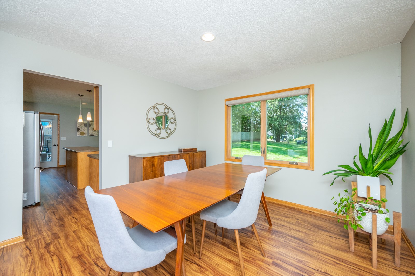 Dining room with a wooden table and chairs, wood-look floors, and a window overlooking the backyard.