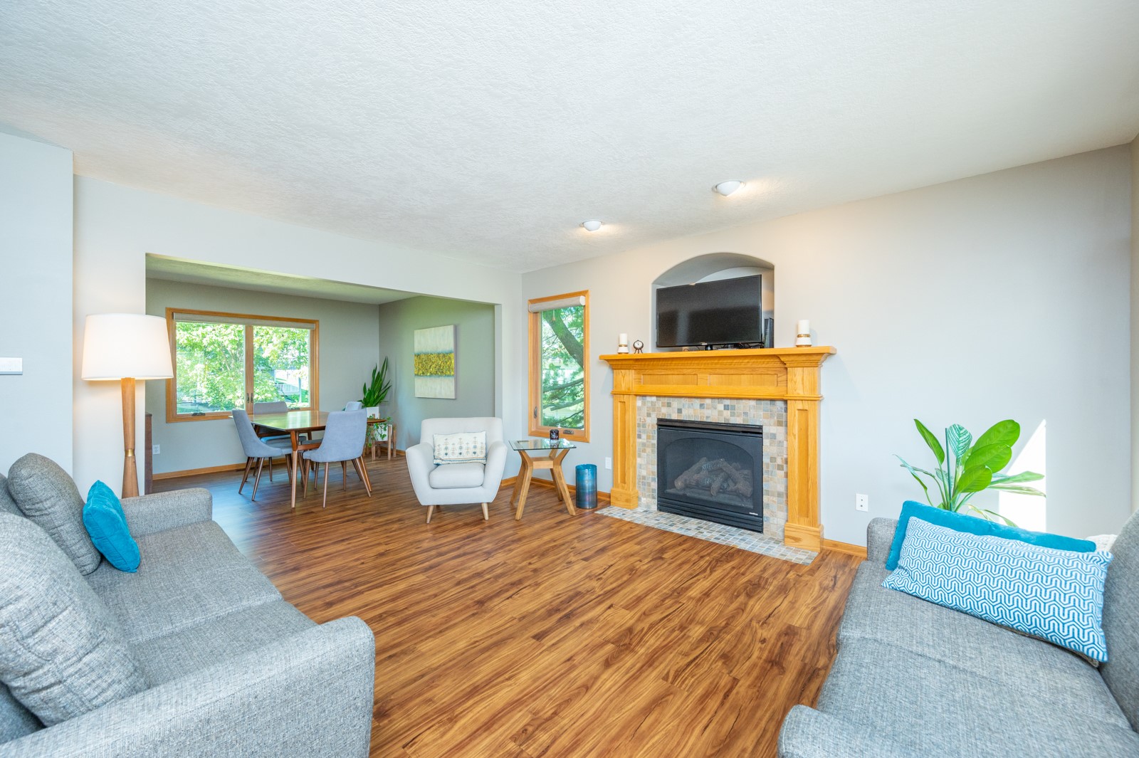 Living room with a tiled fireplace, mounted TV, gray sofas, and adjoining dining area.
