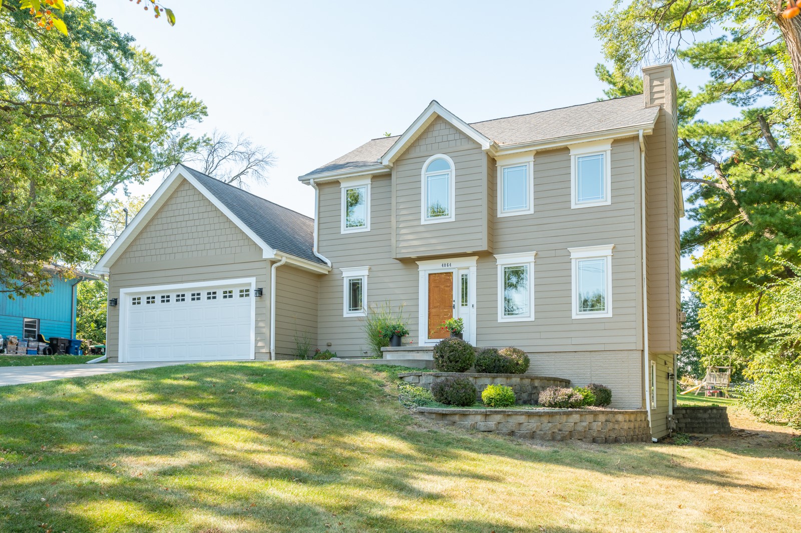 Two-story taupe house with a white garage, front porch, and landscaped lawn.