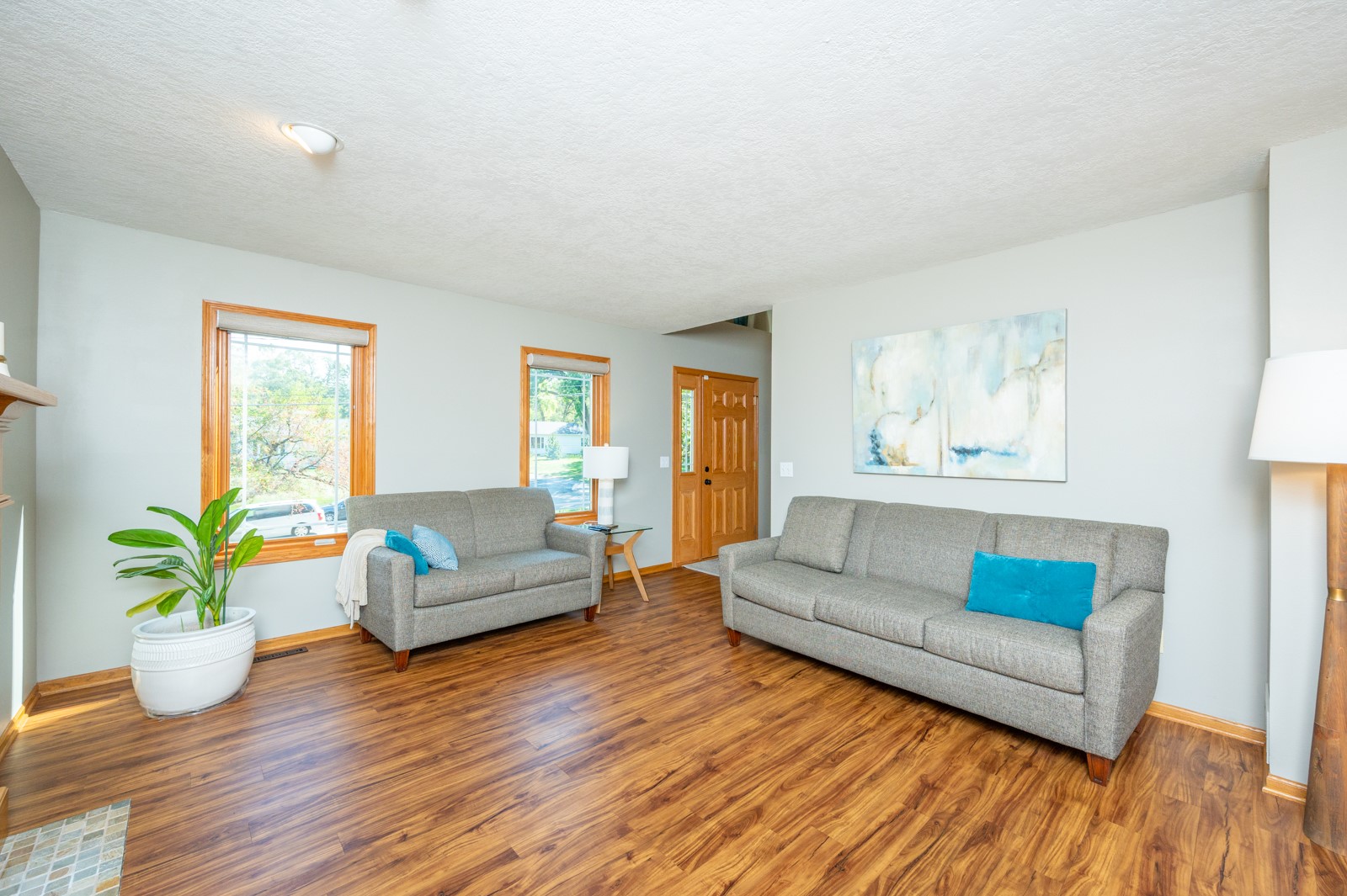 Living room with gray sofas, warm wood flooring, wood-trimmed windows, and abstract wall art.