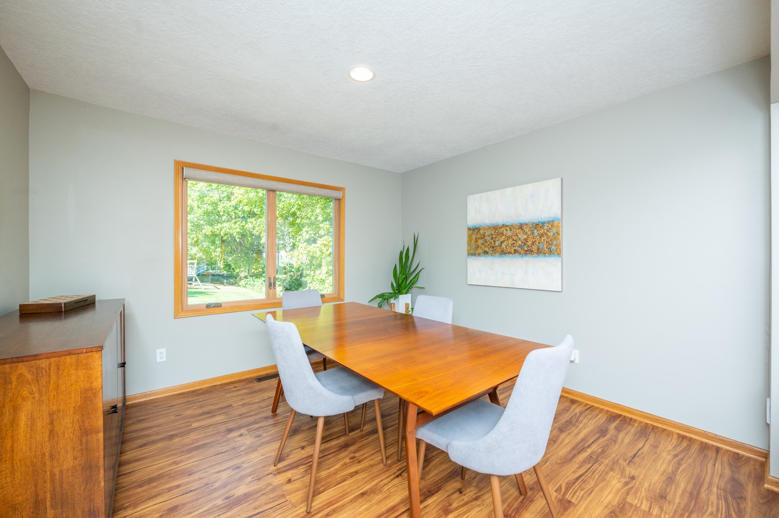 Dining room with a long wooden table, pale chairs, and a window overlooking greenery.