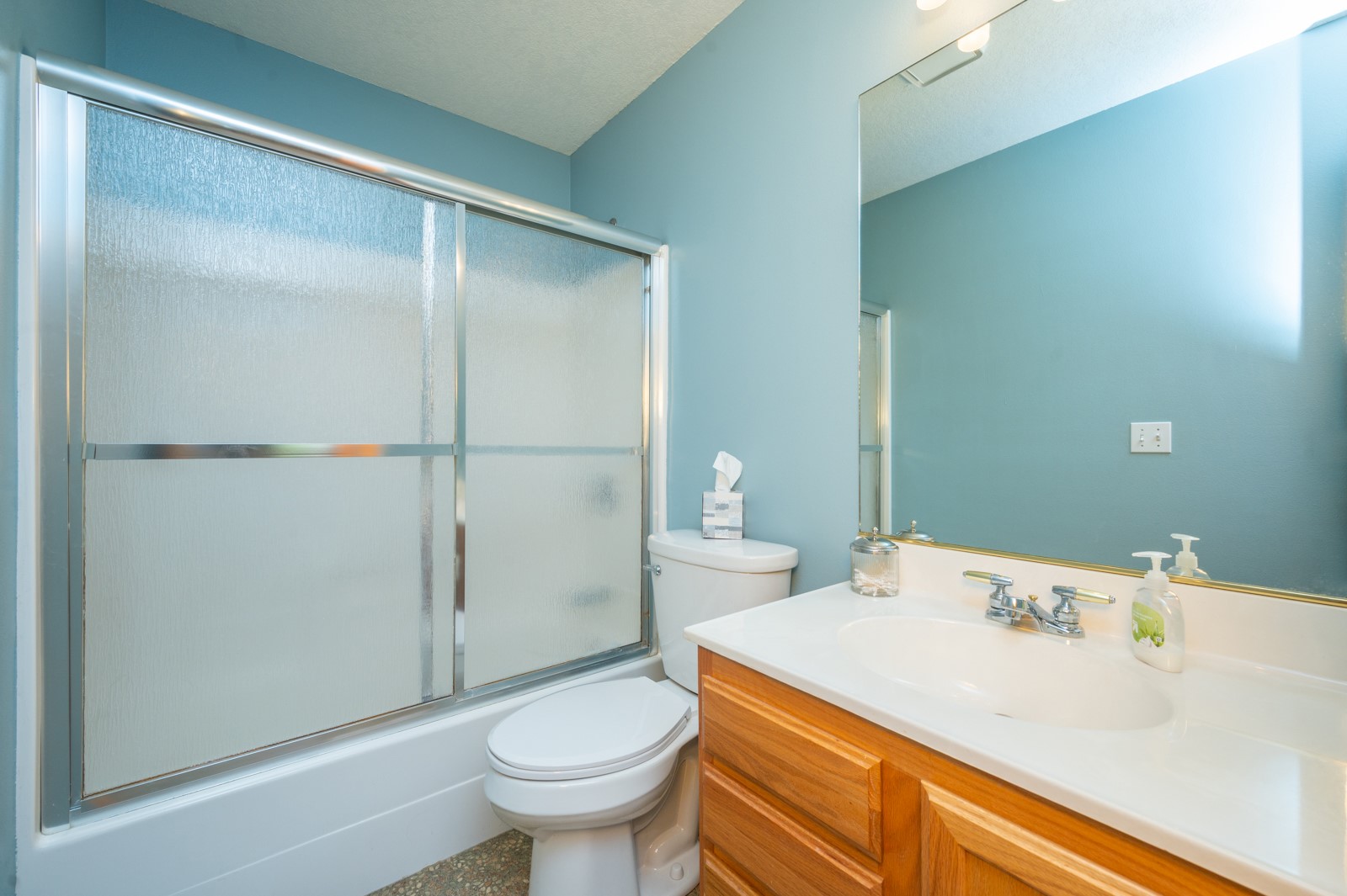 Bathroom with frosted-glass shower doors, a wood vanity, and light blue walls.