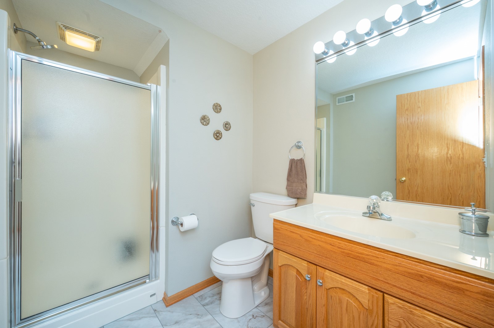Bathroom with frosted-glass shower, toilet, and oak vanity beneath a large lit mirror.