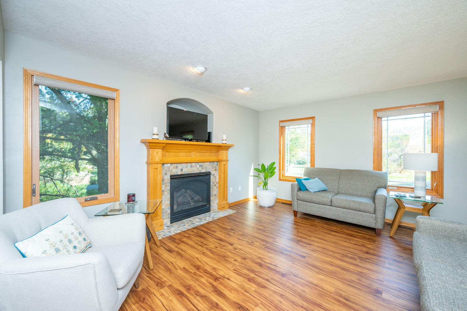 Living room with a tiled fireplace, wood floors, large windows, and gray and white sofas.