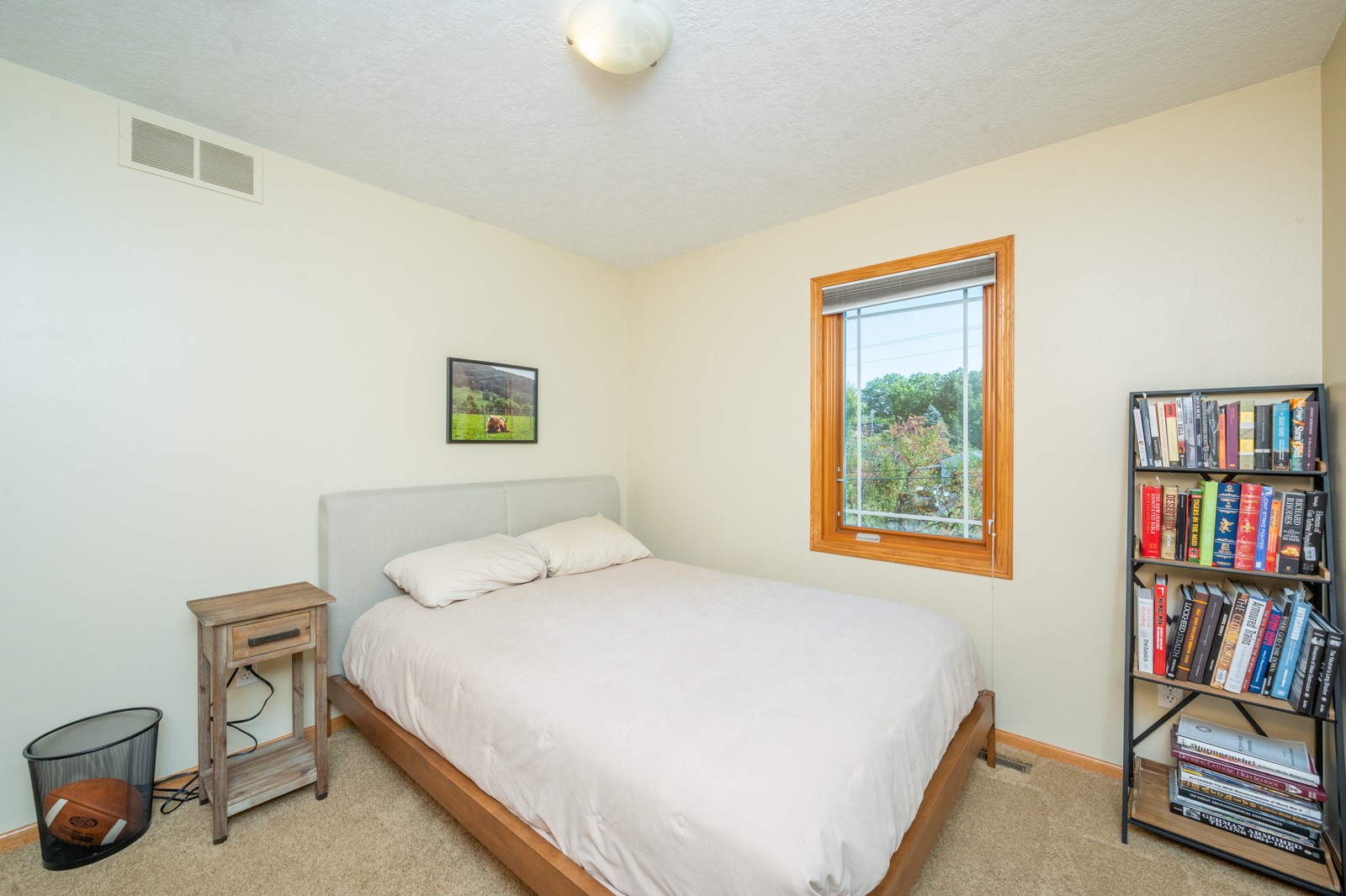 Bedroom with a white bed, wood-trimmed window, and tall bookcase.