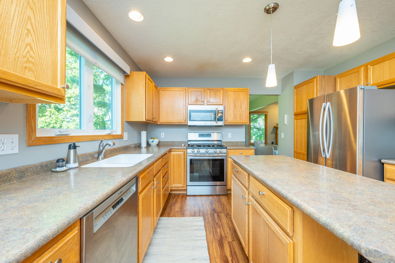 Kitchen with honey-colored cabinets, stainless steel appliances, and a large window overlooking trees.