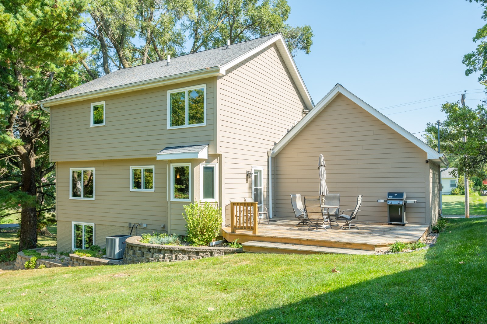 Rear of a beige two-story home with a raised deck, outdoor dining set, and barbecue grill.