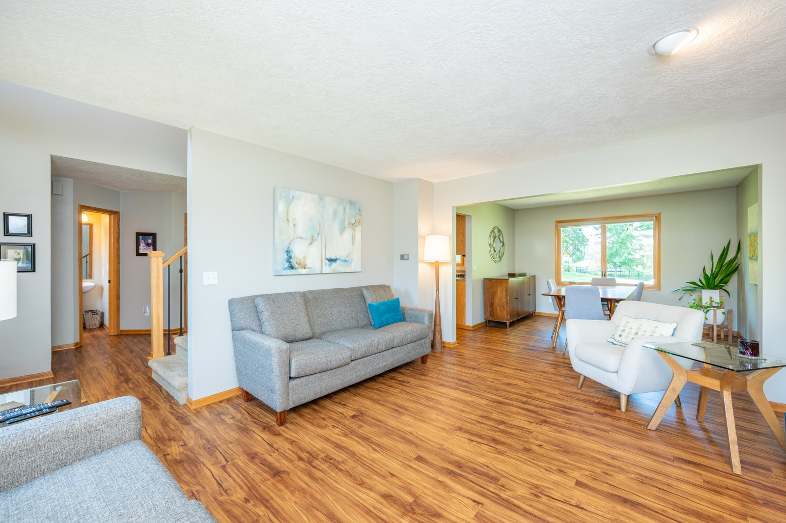 Living room with a gray sofa and wood-look floors opening into a bright dining area.