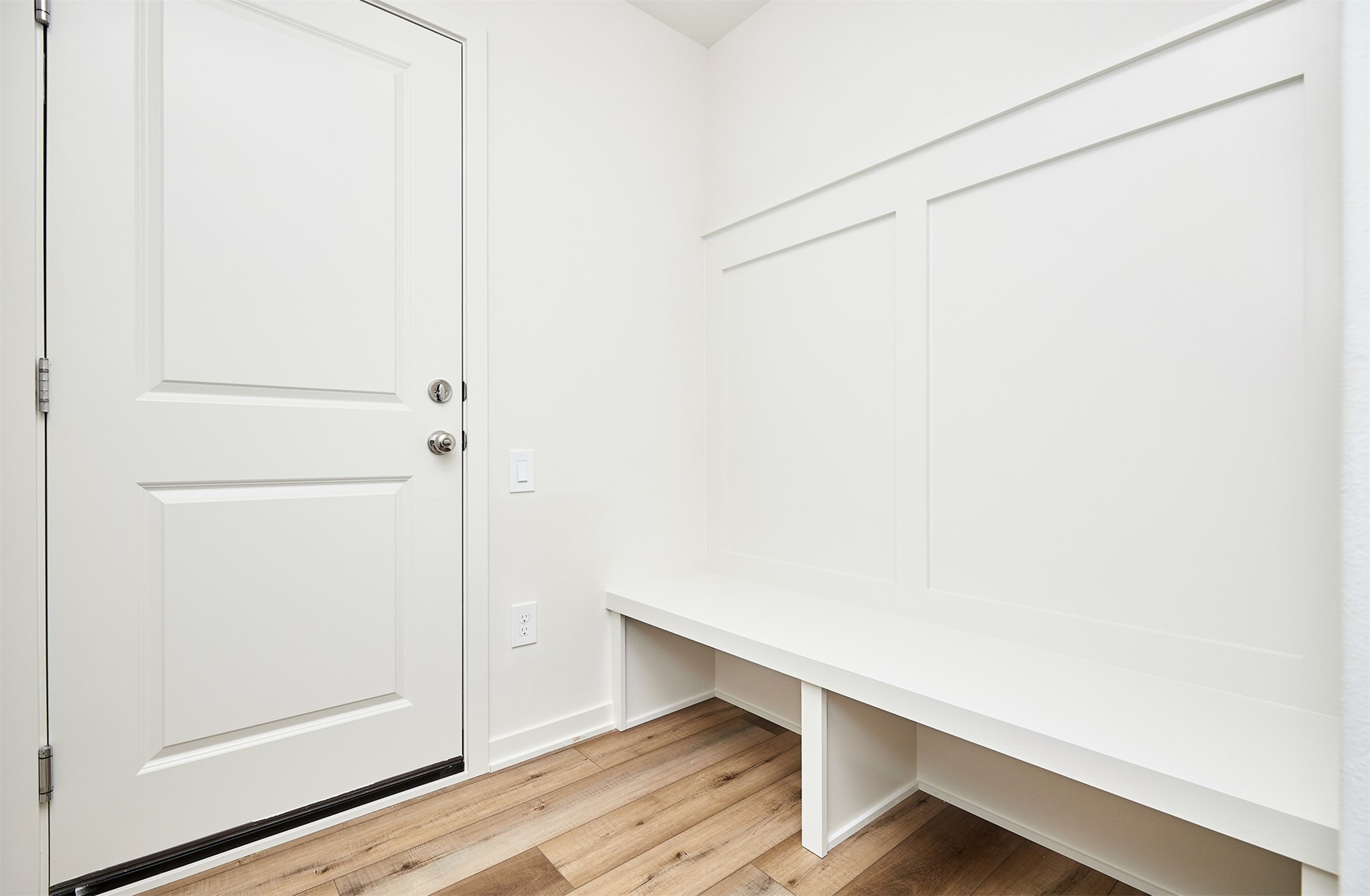 Entryway with a white paneled door, built-in bench and cubbies, and wood-look flooring.