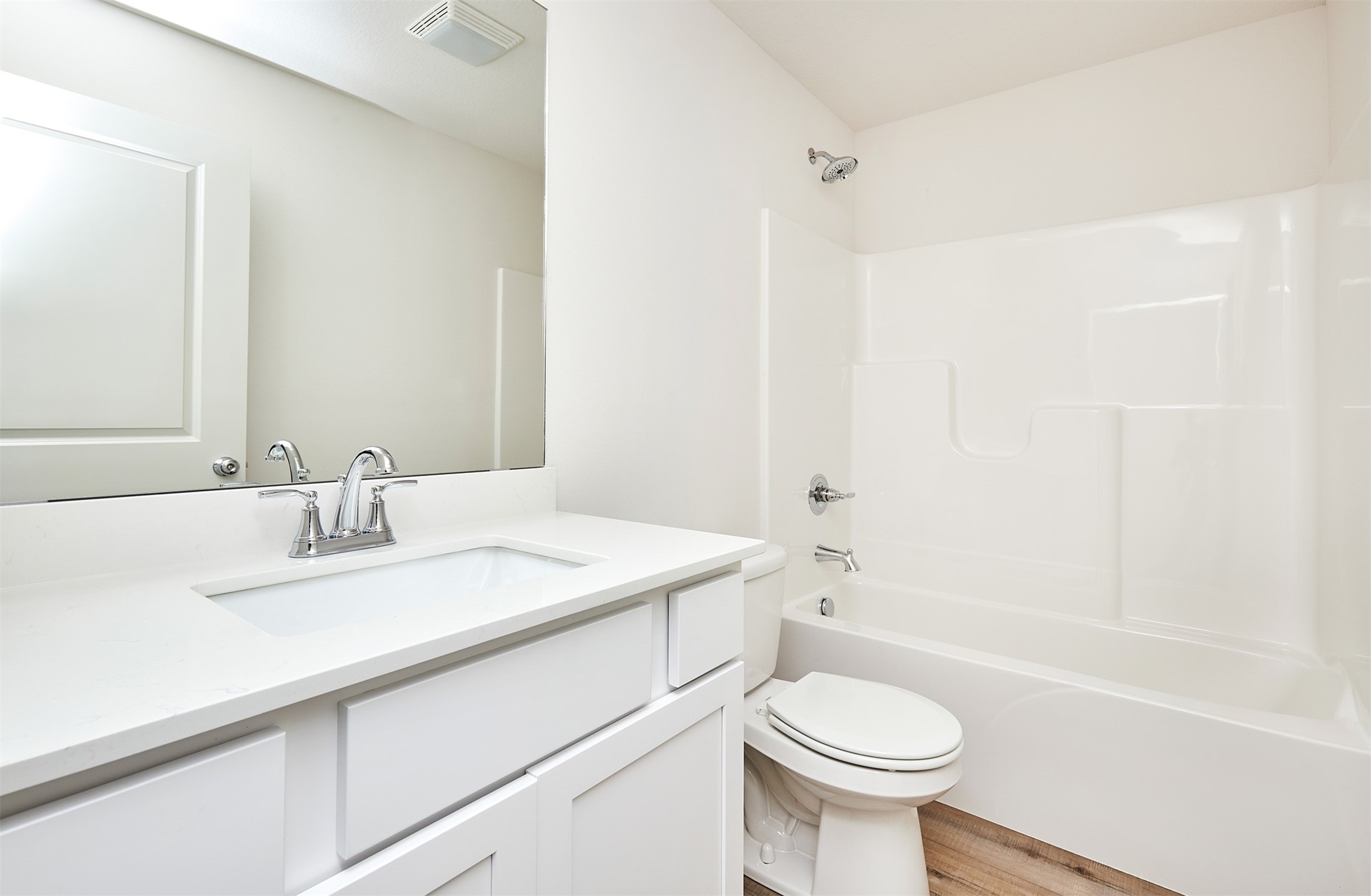 Bathroom with a white vanity and large mirror beside a tub-shower and toilet.