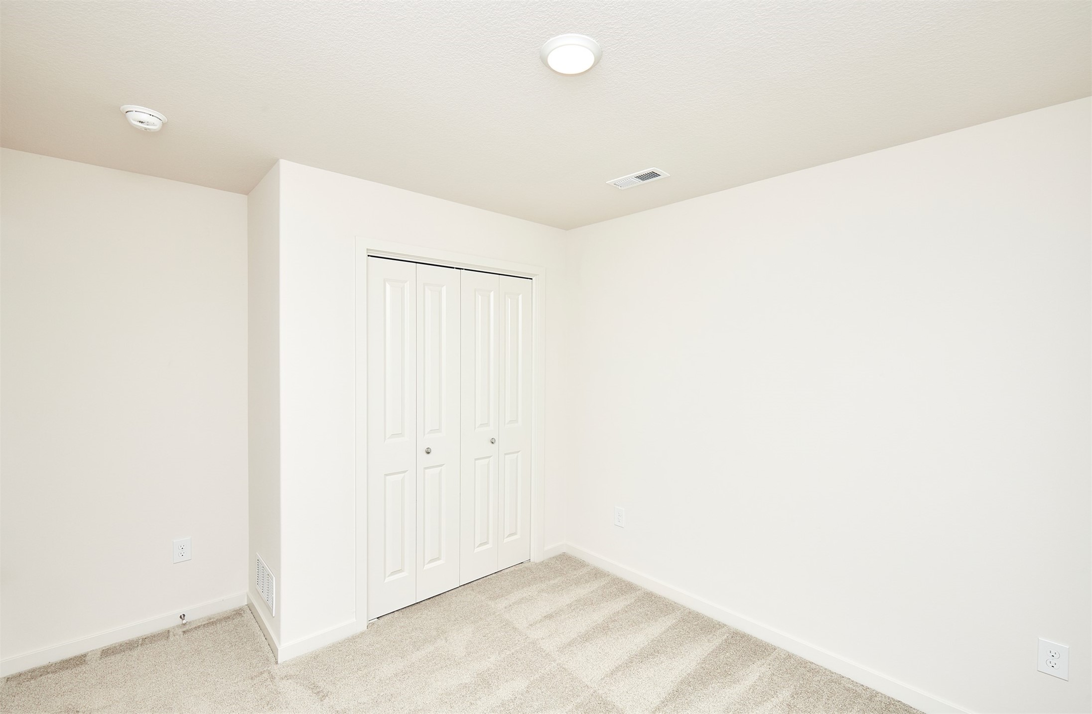 Empty carpeted room with white walls and double closet doors.