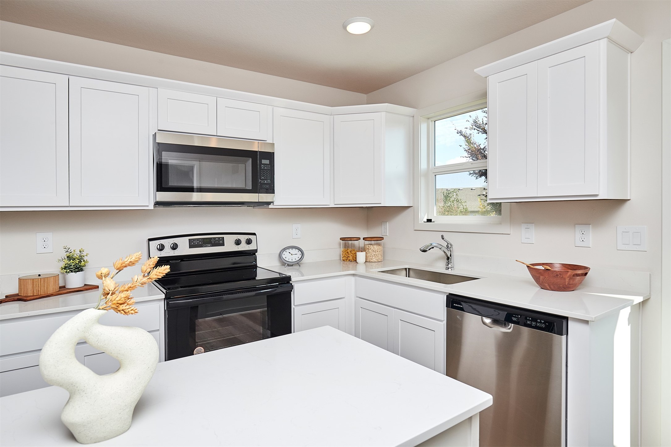 Bright white kitchen with a large island, stainless steel appliances, and a window above the sink.