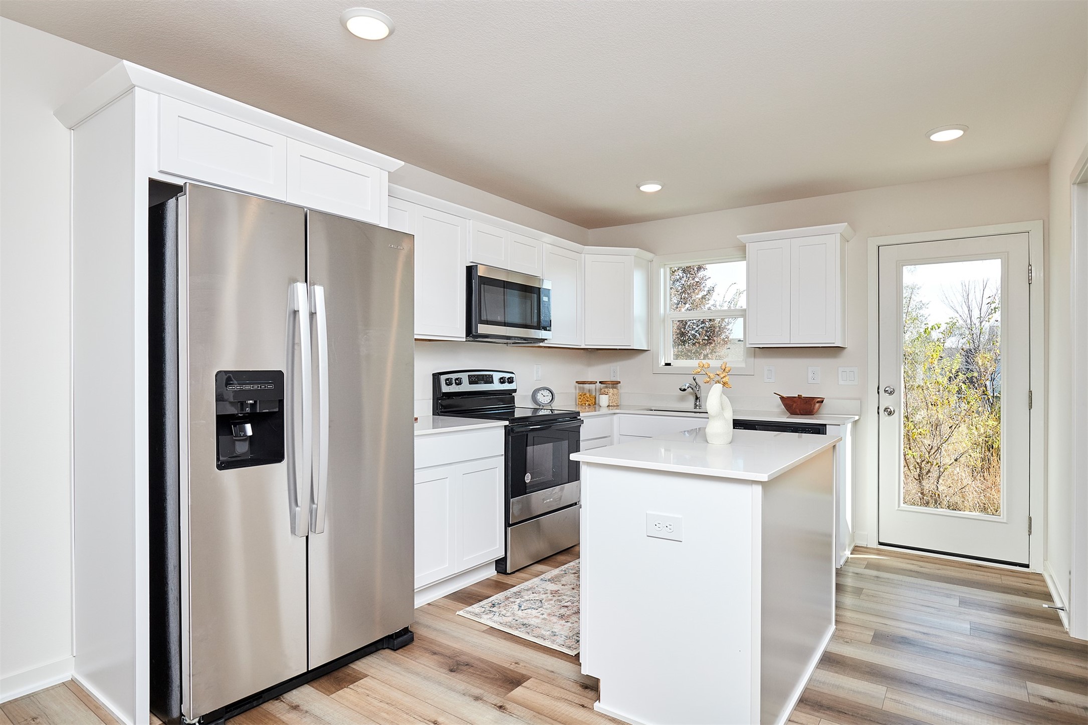 Bright white kitchen with a central island, stainless steel appliances, and a glass-panel door.