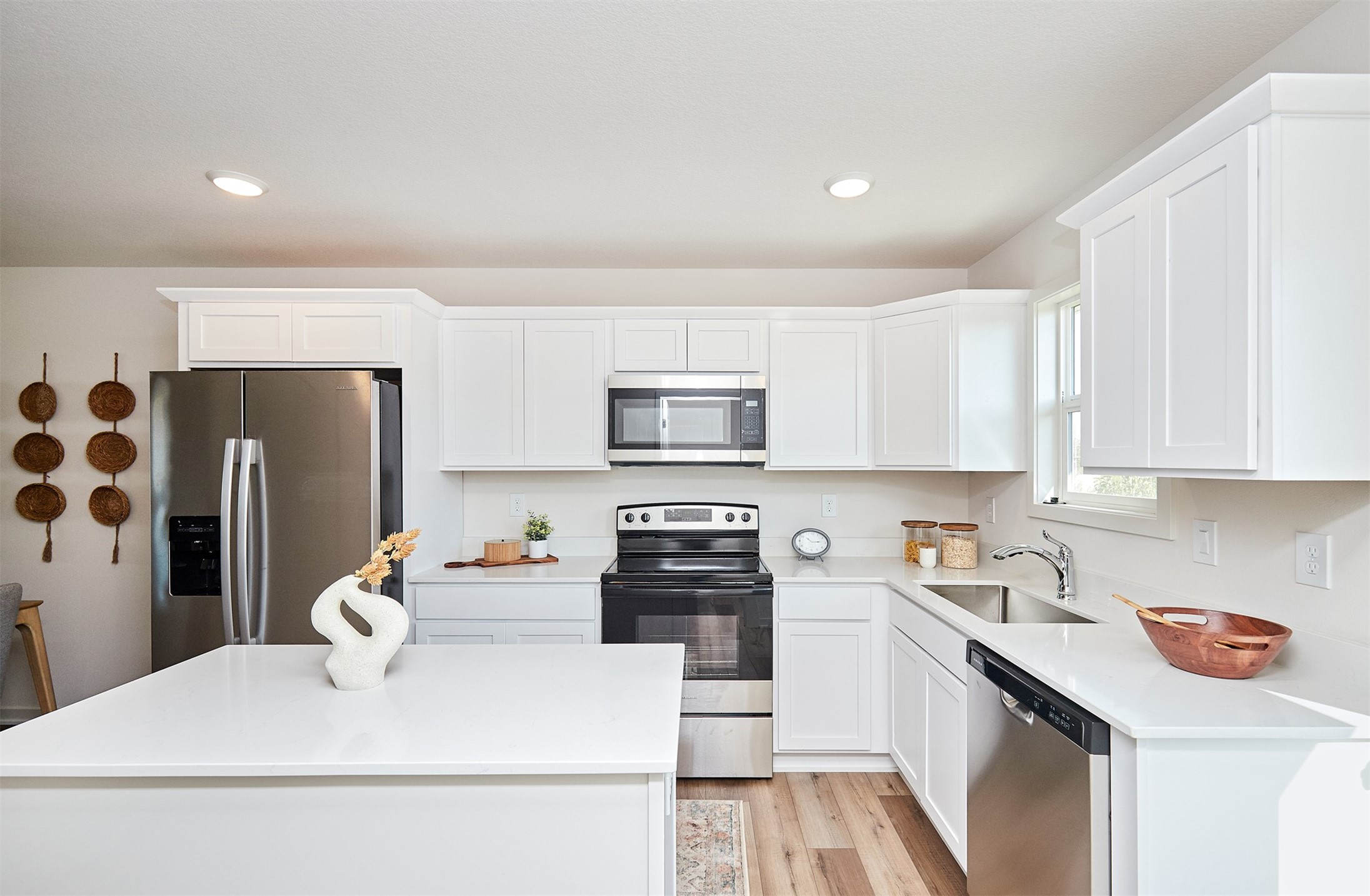 Bright white kitchen with a large island, stainless steel appliances, and wood-look floors.