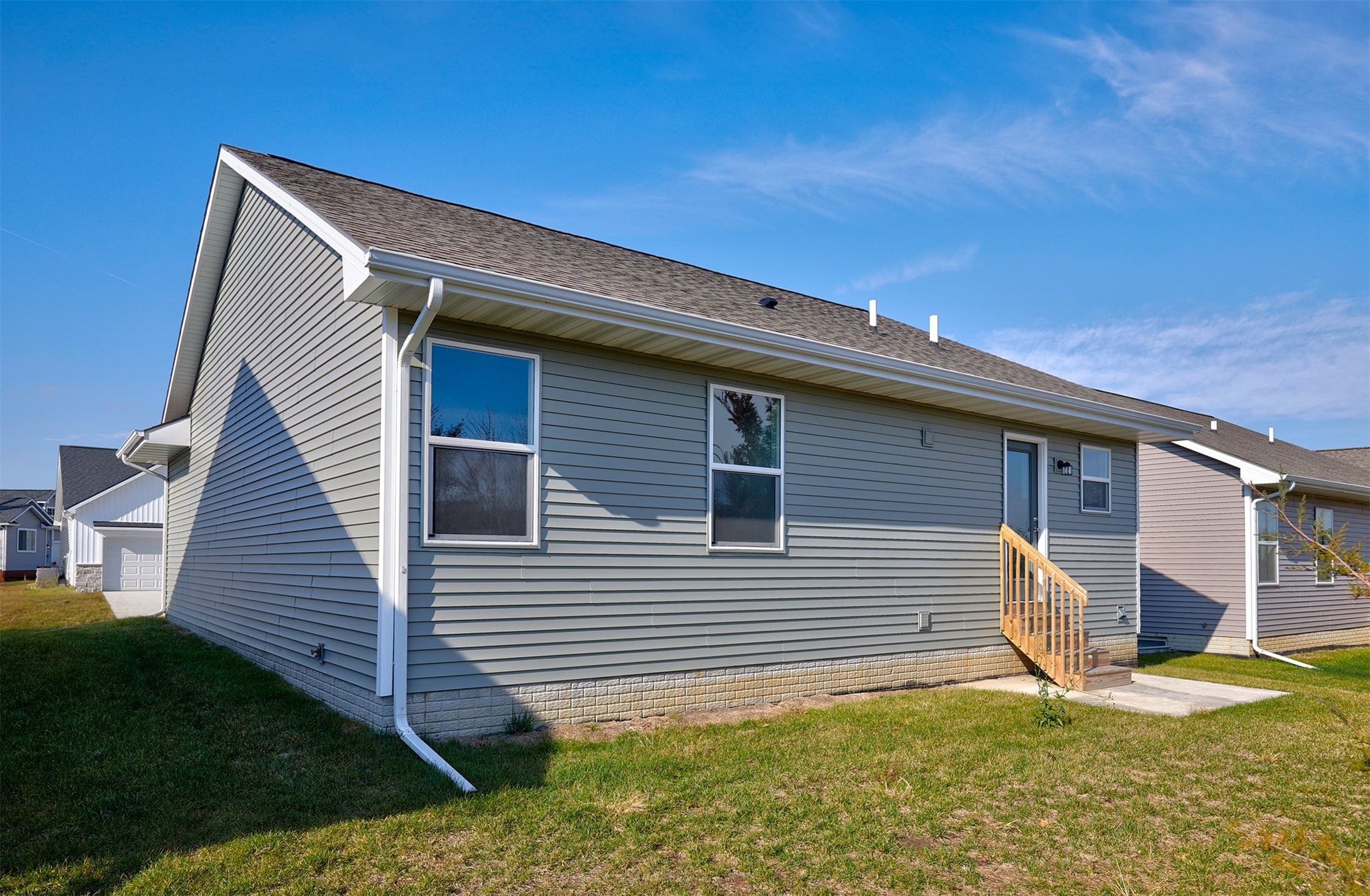 Gray-sided home with white trim and wooden steps to a side entrance, beside a lawn.