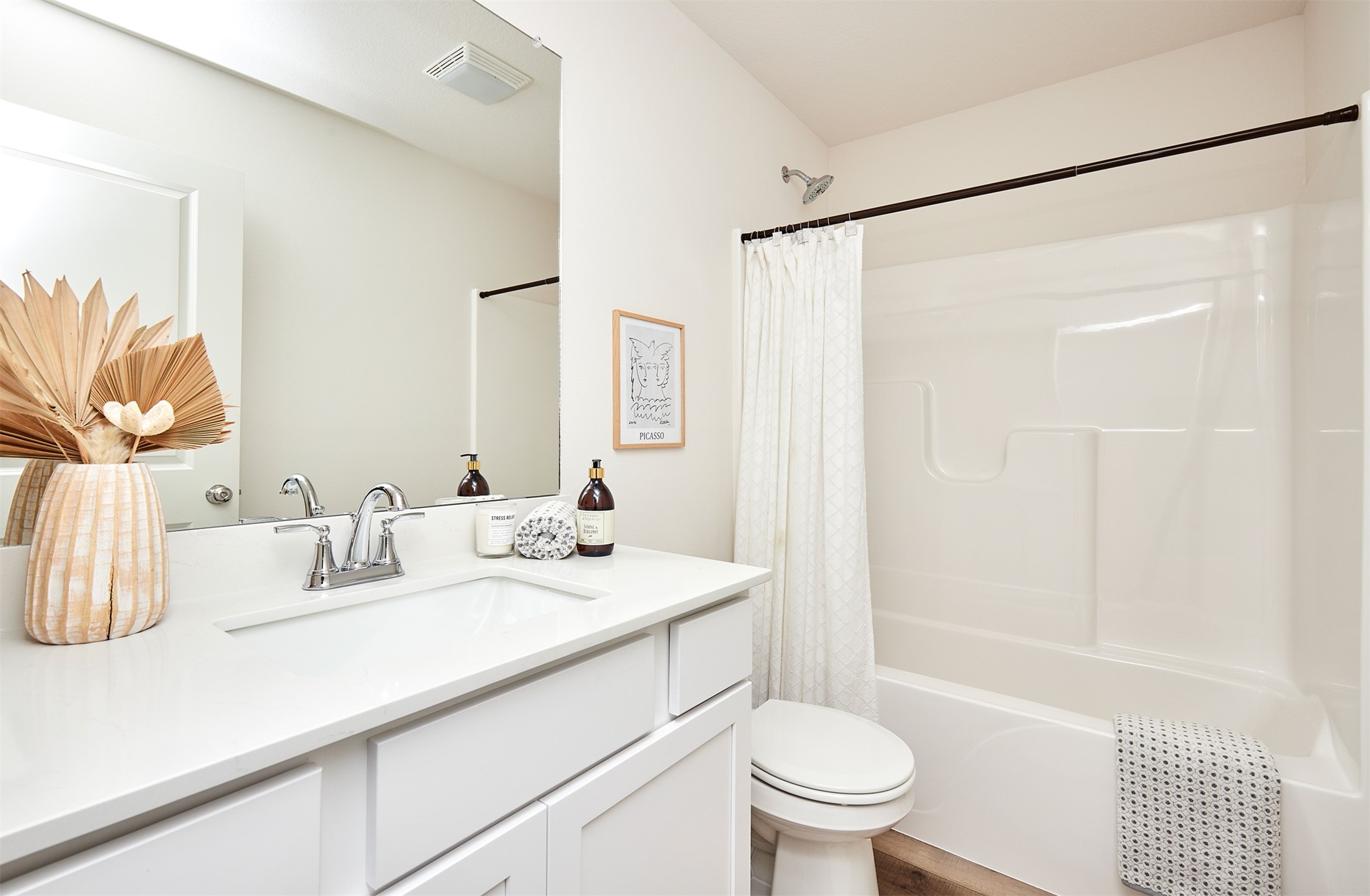 Bright bathroom with a white vanity, large mirror, and bathtub-shower behind a white curtain.
