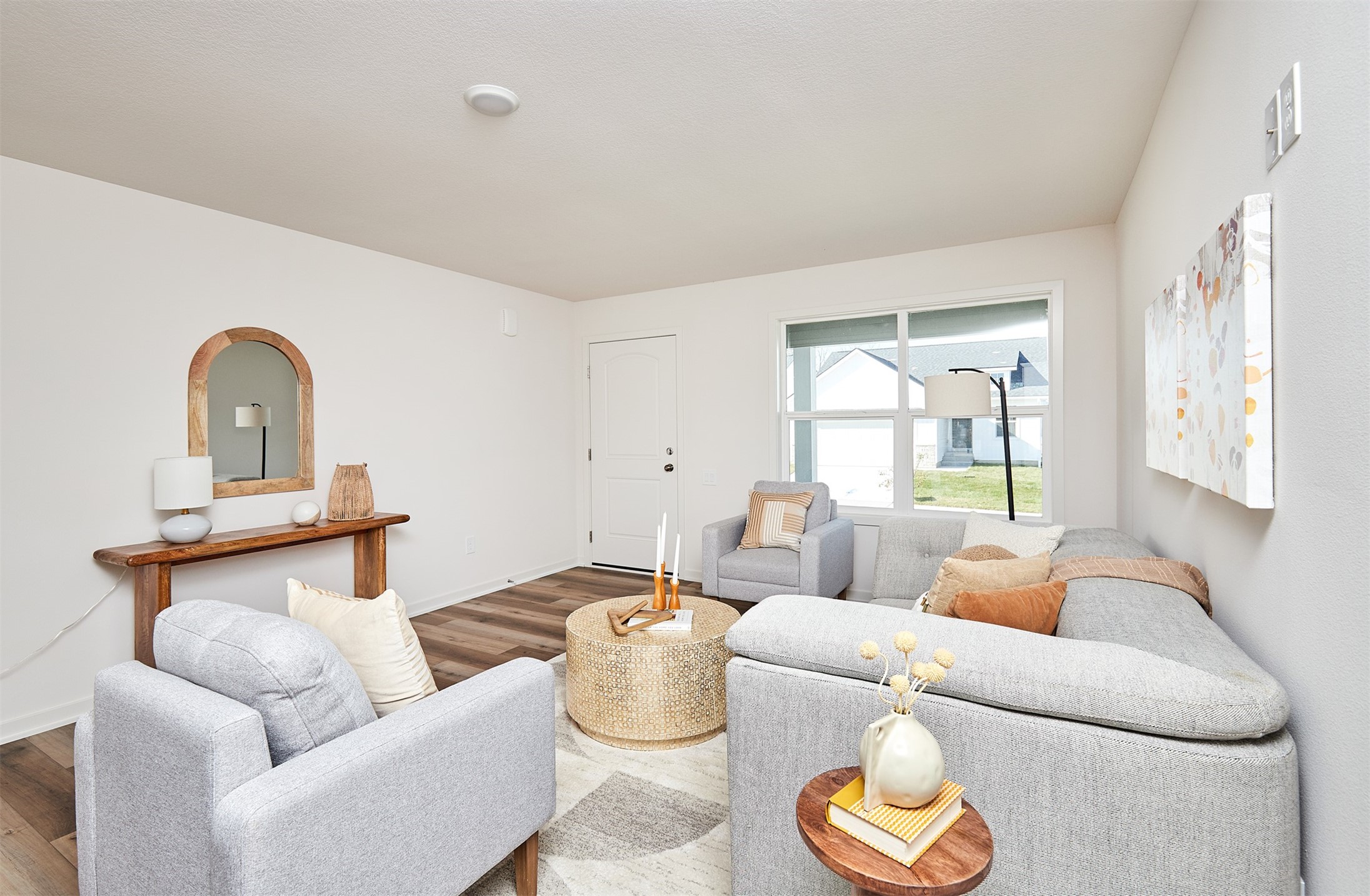 Staged living room with gray sectional and armchairs, woven coffee table, and large window.