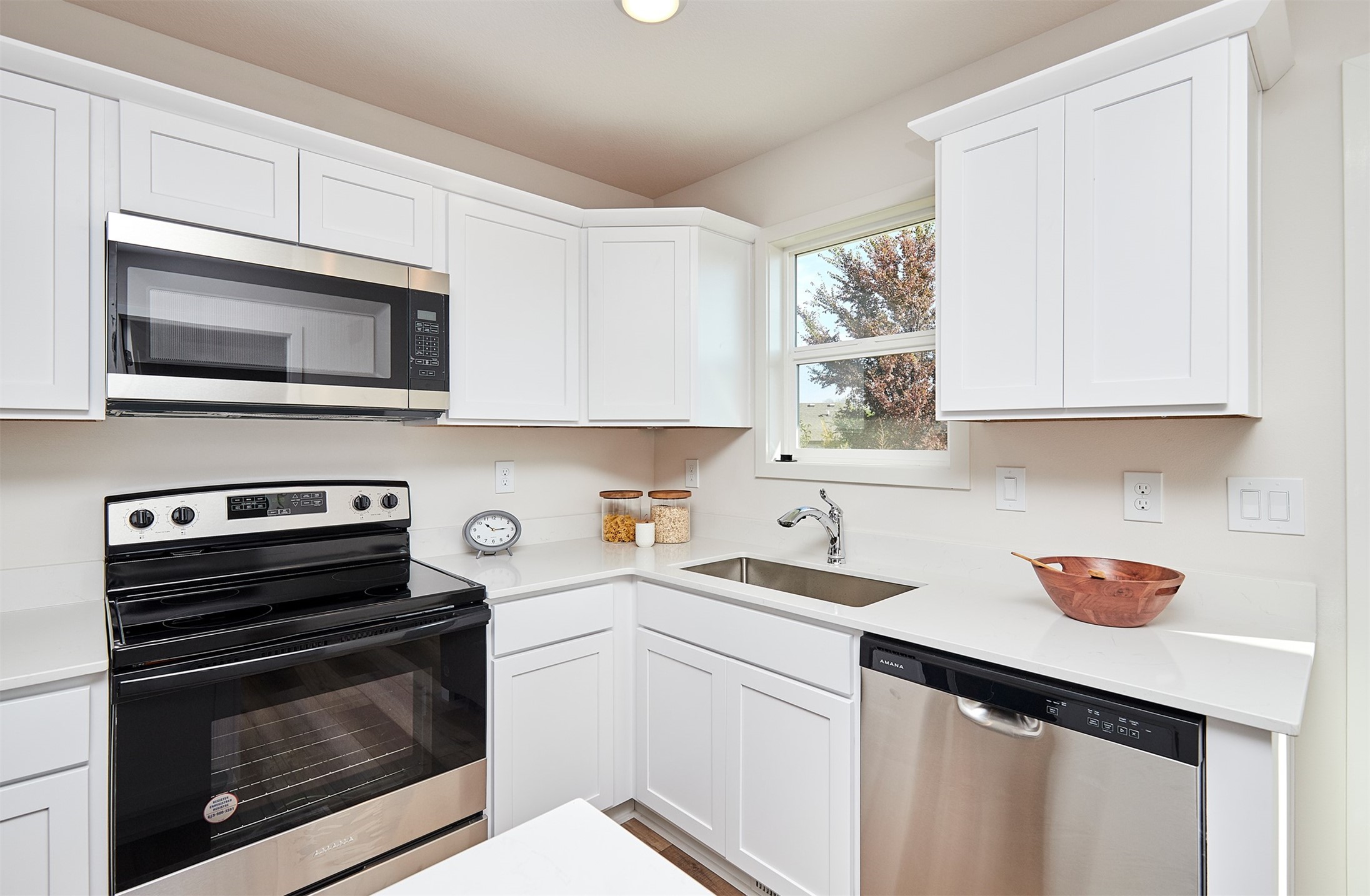 Bright kitchen with white cabinets, black range, stainless dishwasher, and a window above the sink.