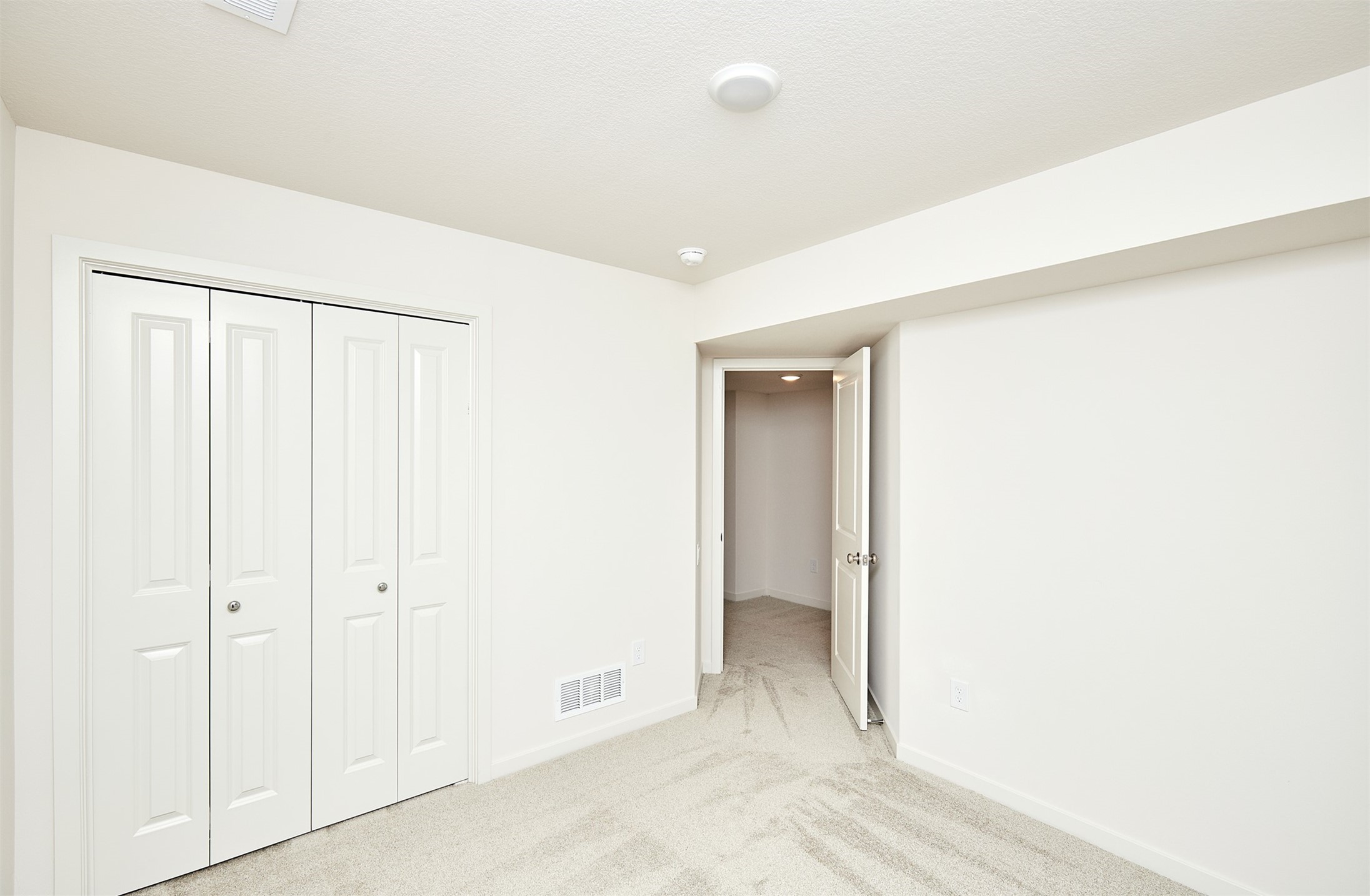 Empty carpeted room with a four-panel closet and an open doorway.