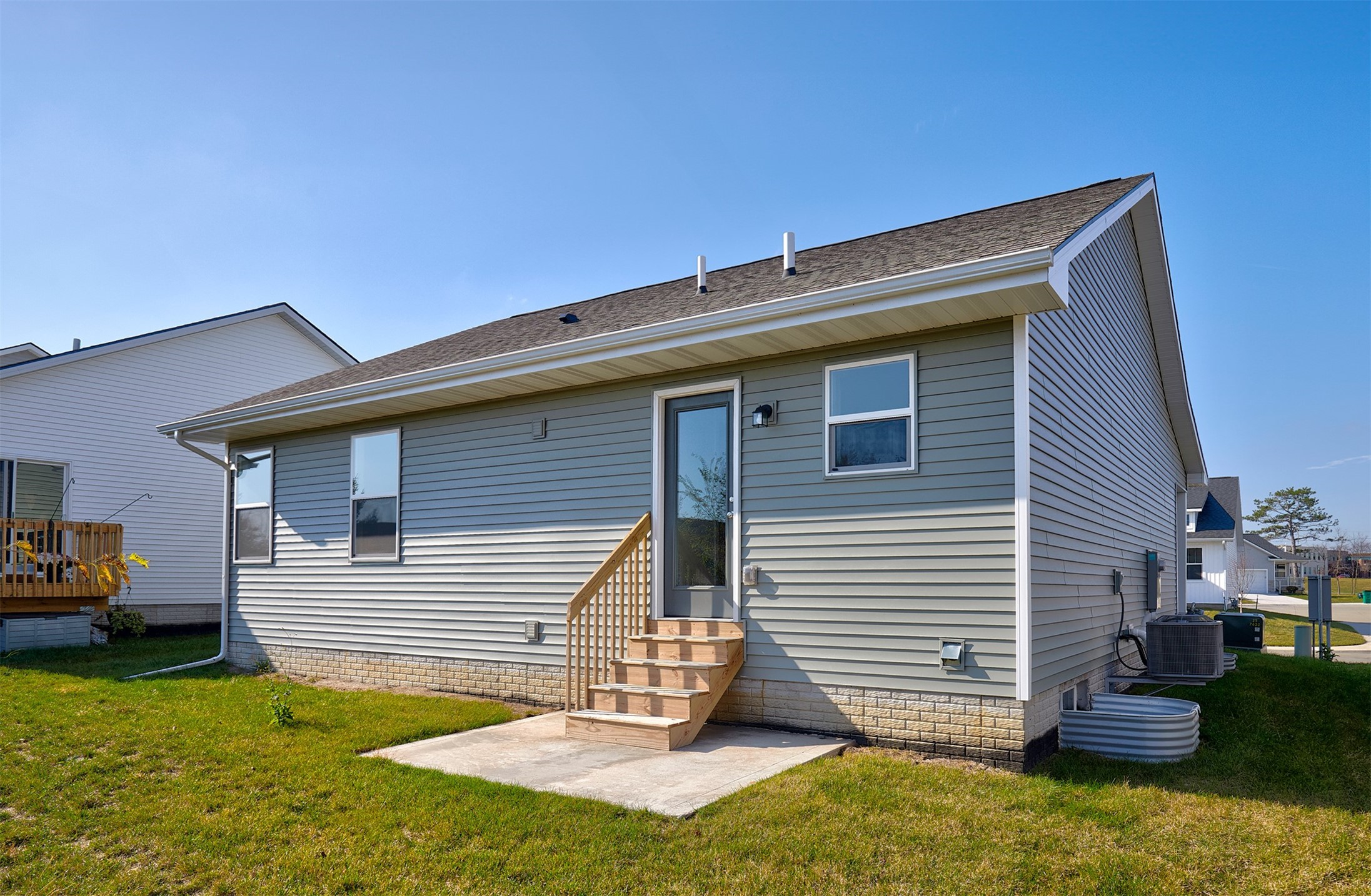 Rear exterior of a gray-sided home with wooden back steps, a concrete patio, and a green lawn.