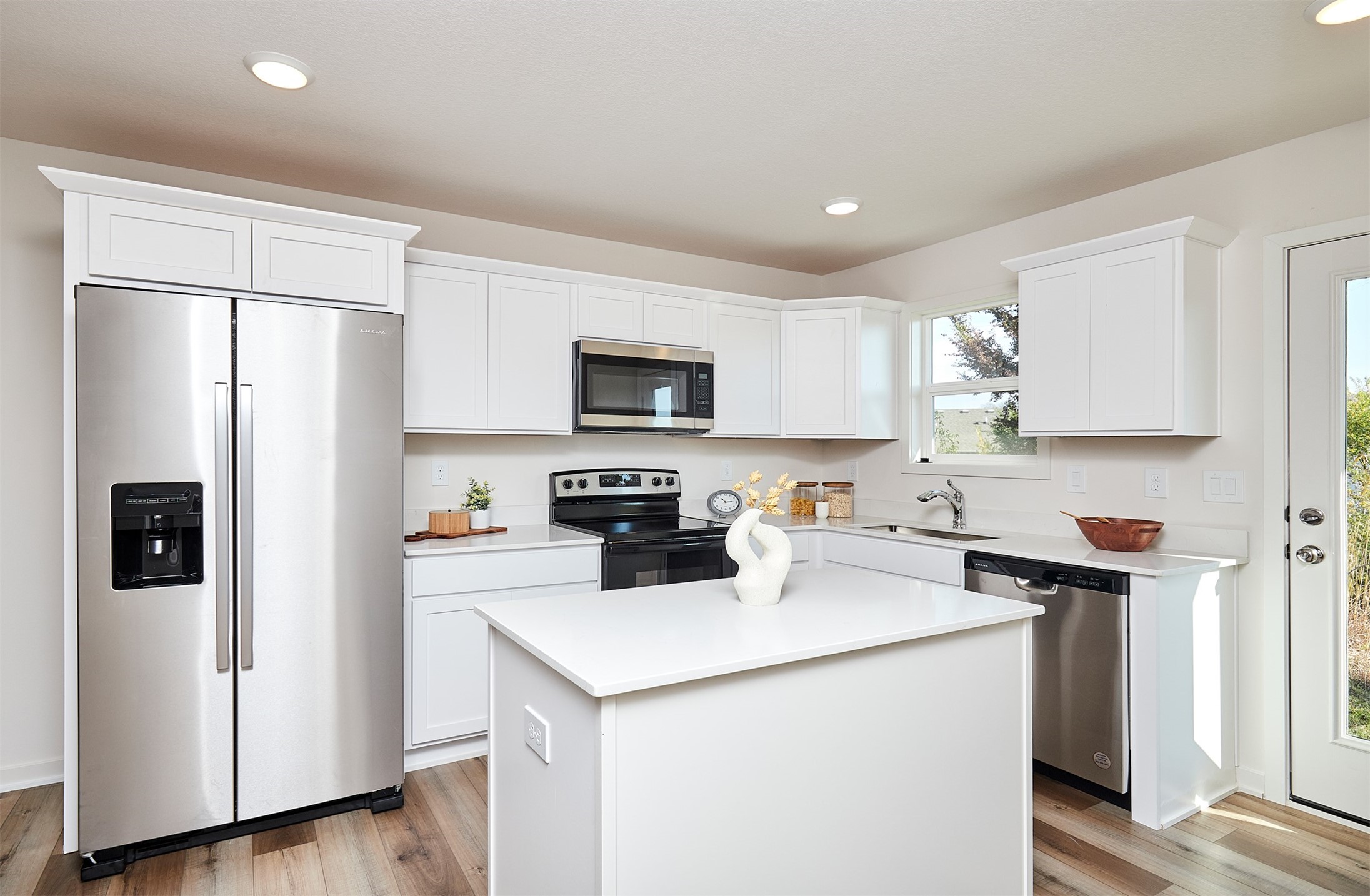 Bright kitchen with a large white island, stainless steel appliances, and white cabinets.