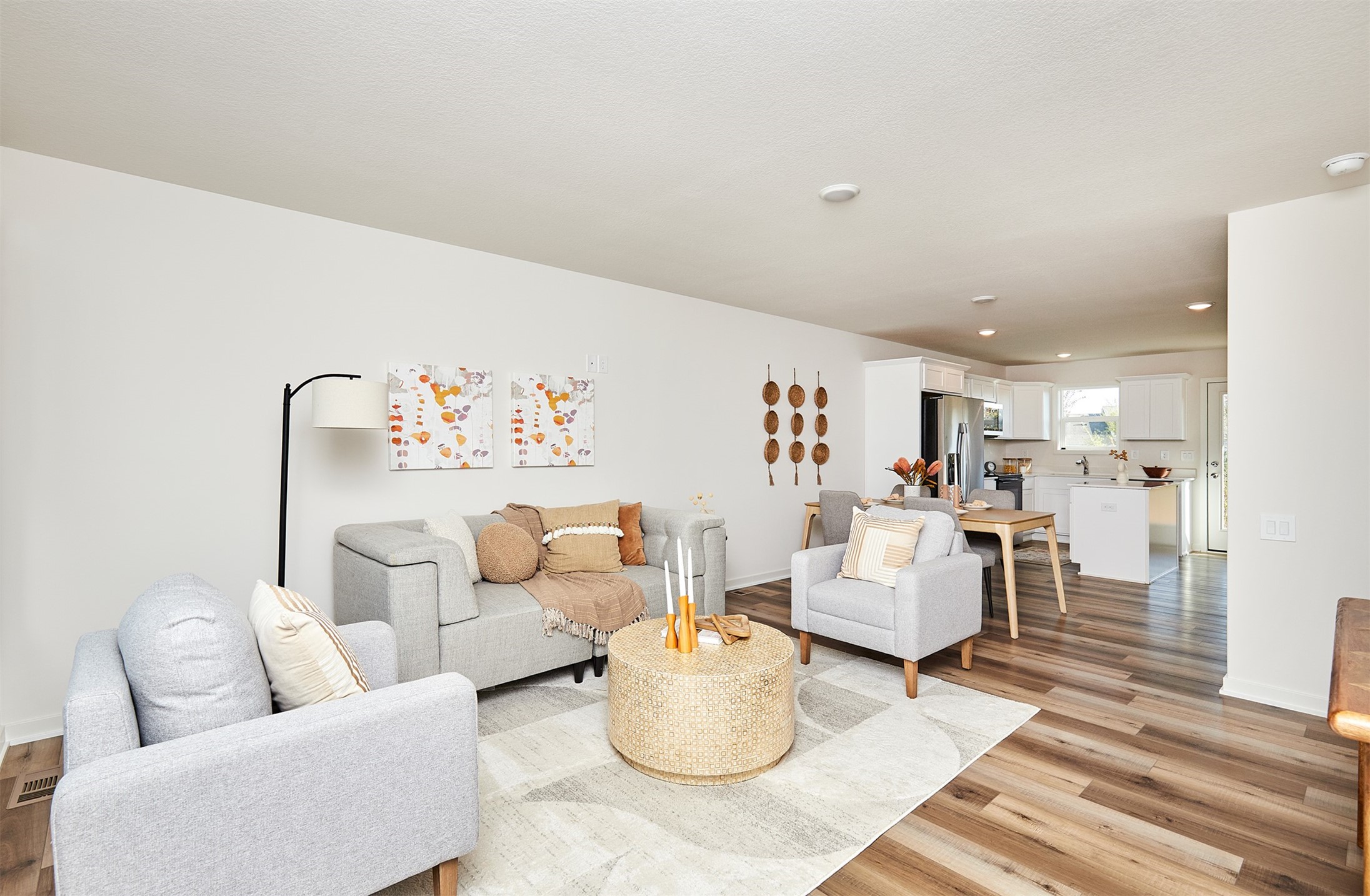Open-plan living room with gray sofas and a woven coffee table leading into a bright white kitchen.