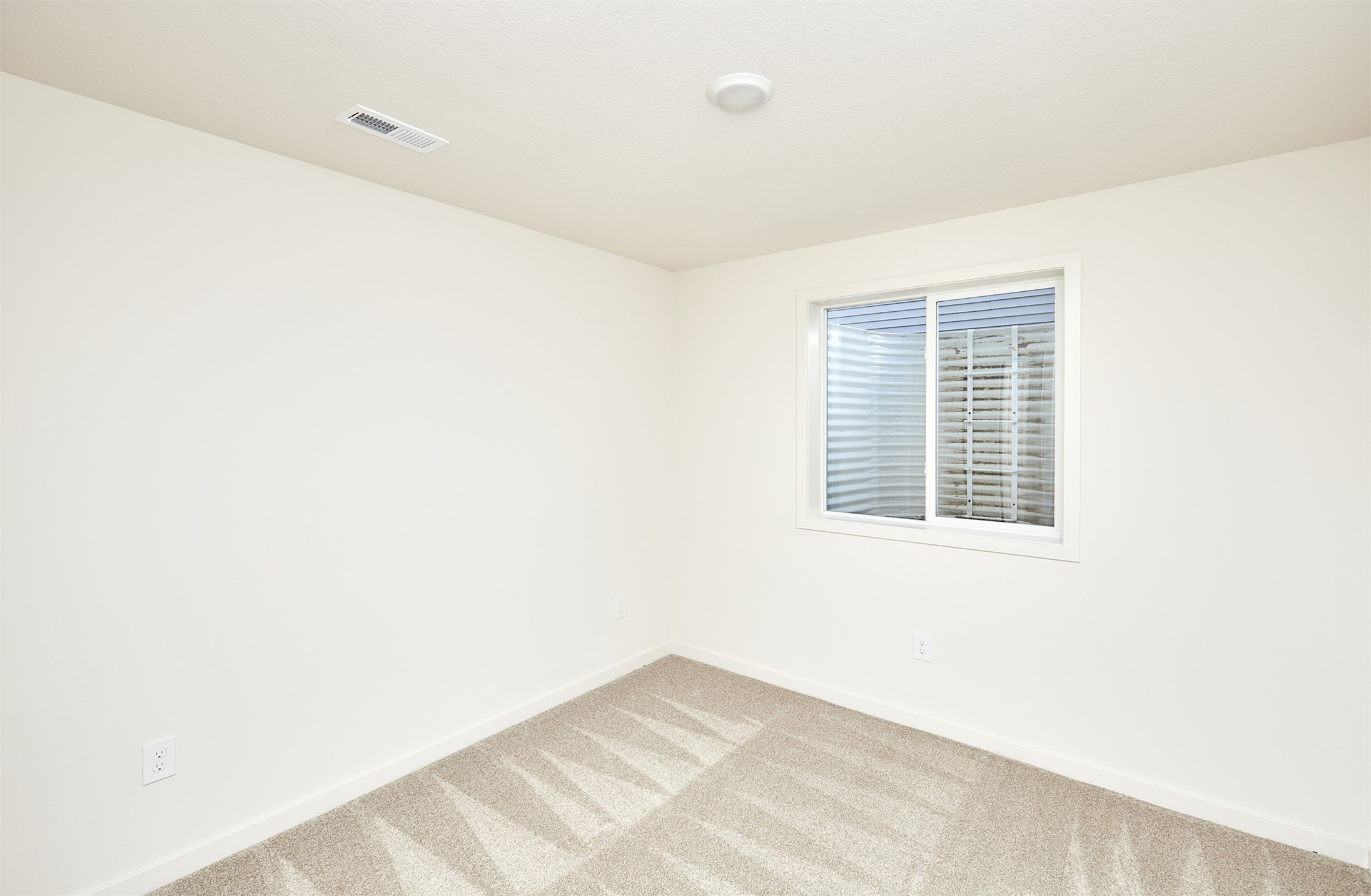 Empty carpeted room with white walls and a small window with blinds.