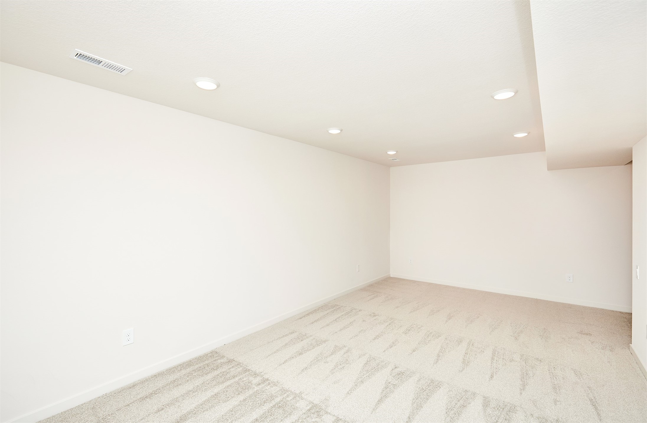 Vacant carpeted room with recessed ceiling lights and a ceiling air vent.