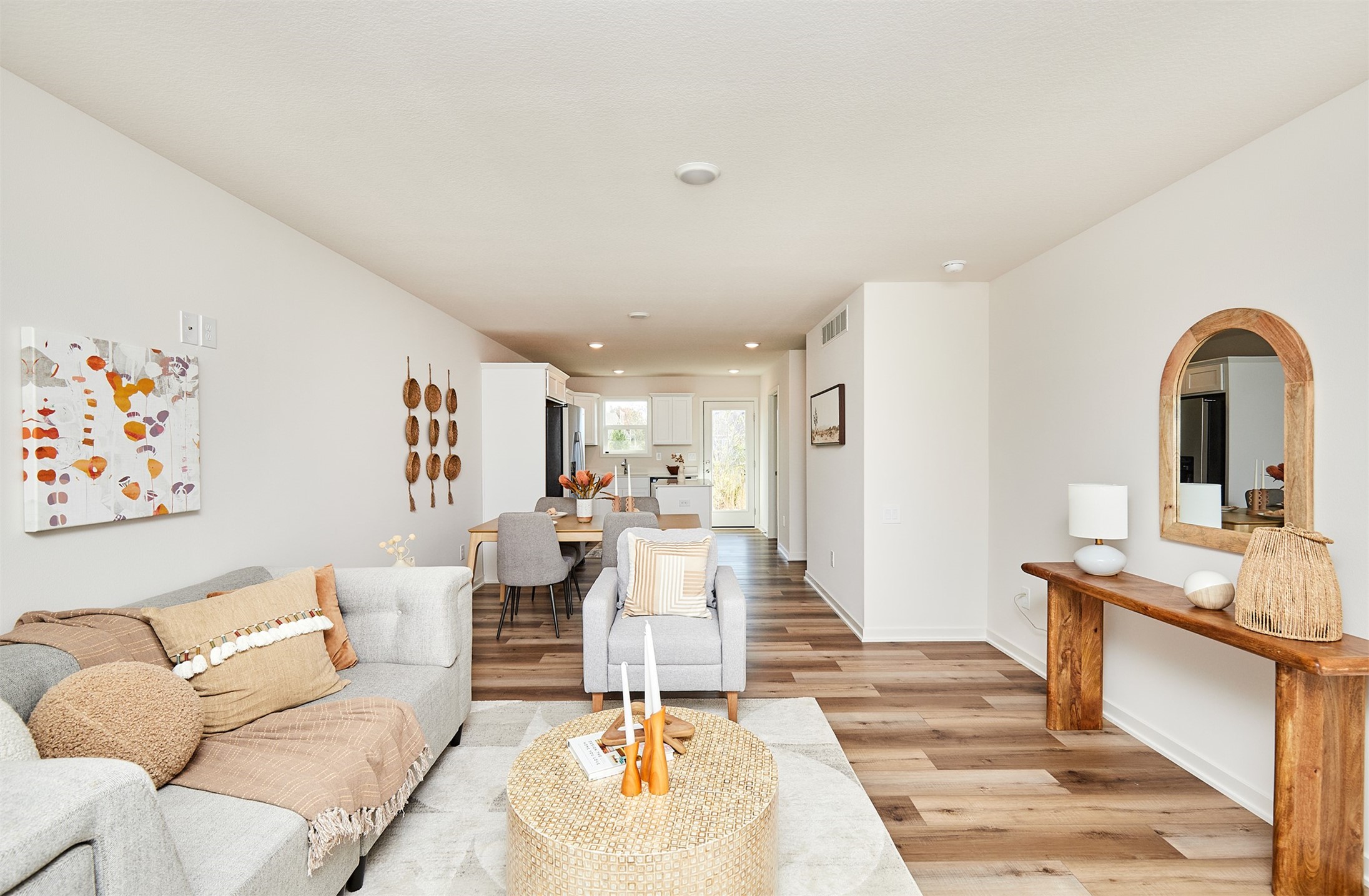 Open-plan living room with gray seating, wood-look floors, and a kitchen at the rear.