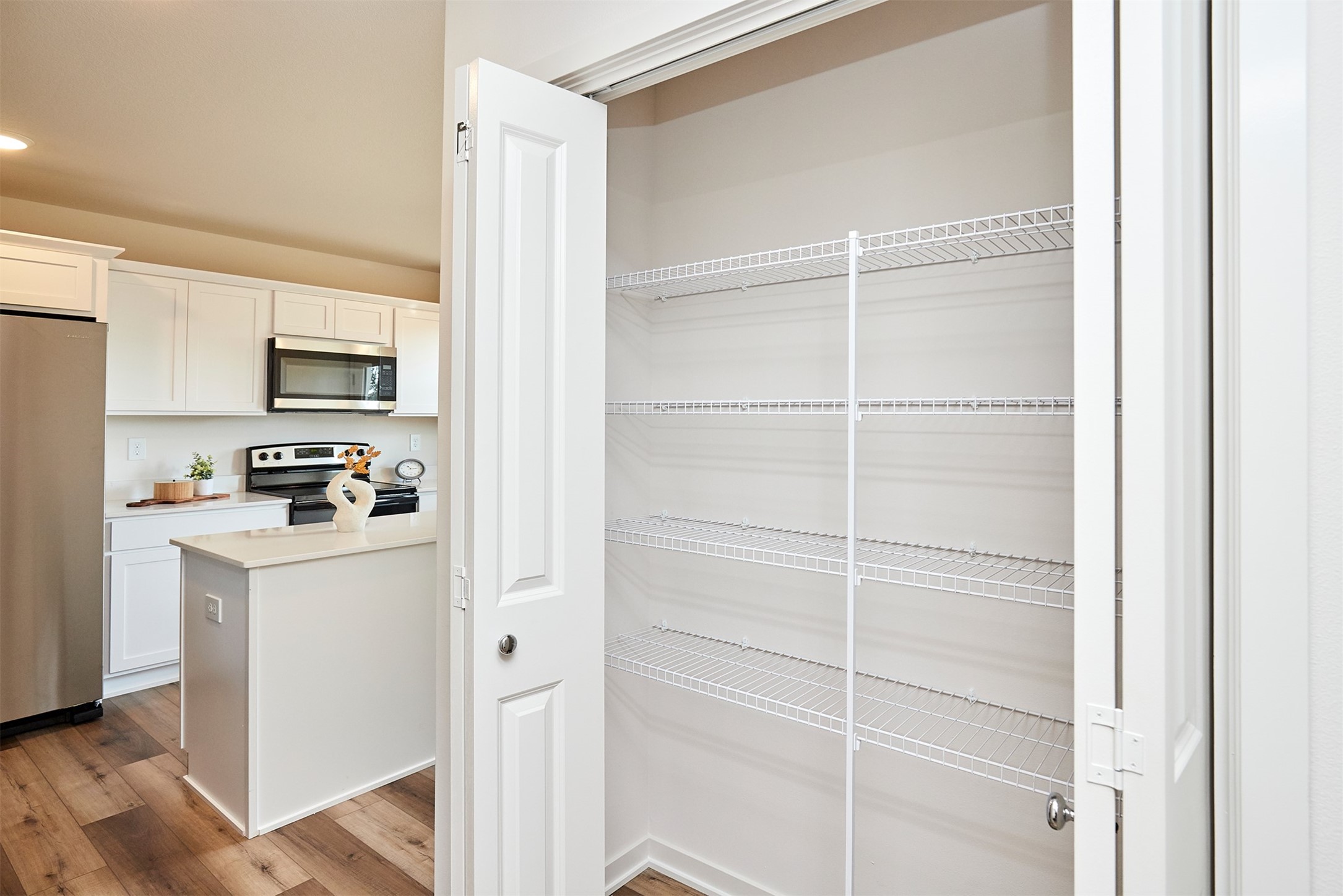 Walk-in pantry with white wire shelving beside a bright kitchen with an island.