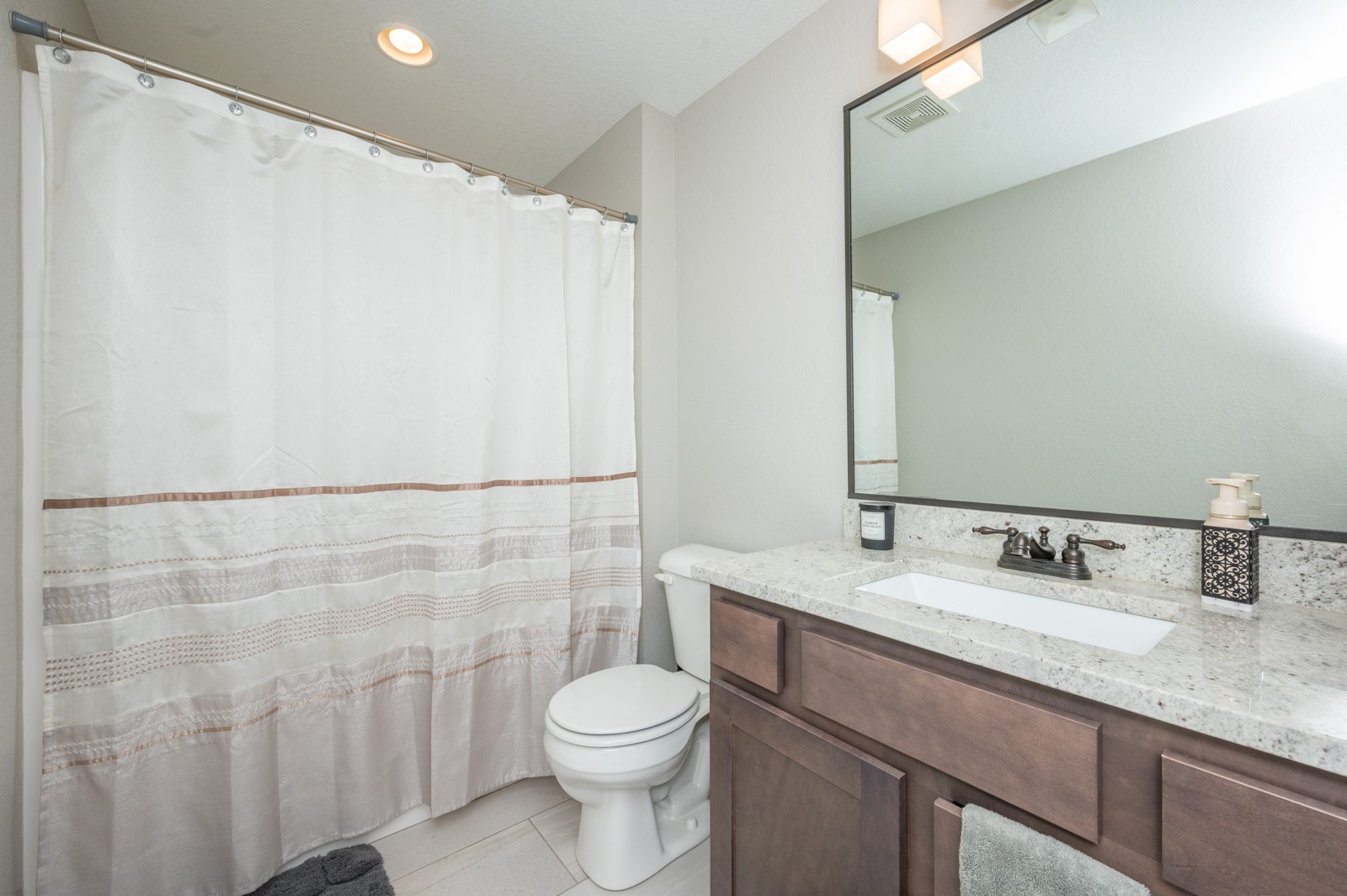 Bathroom with a striped shower curtain and dark wood vanity with a stone countertop.