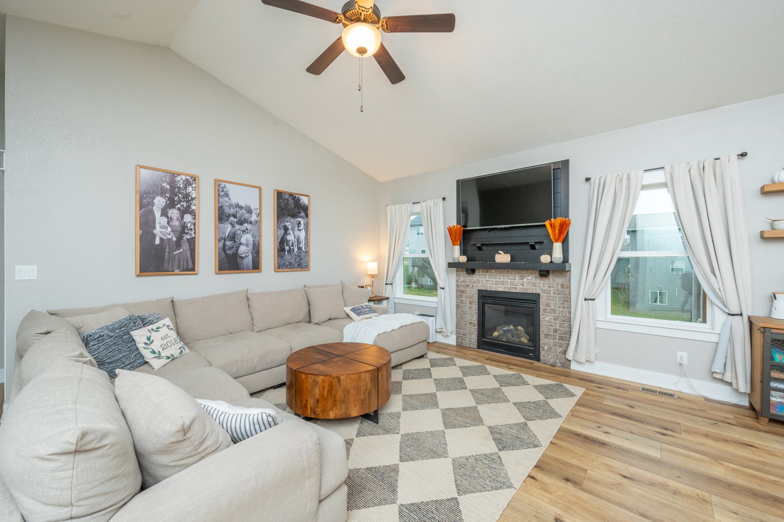 Living room with a vaulted ceiling, sectional sofa, and brick fireplace beneath a mounted television.