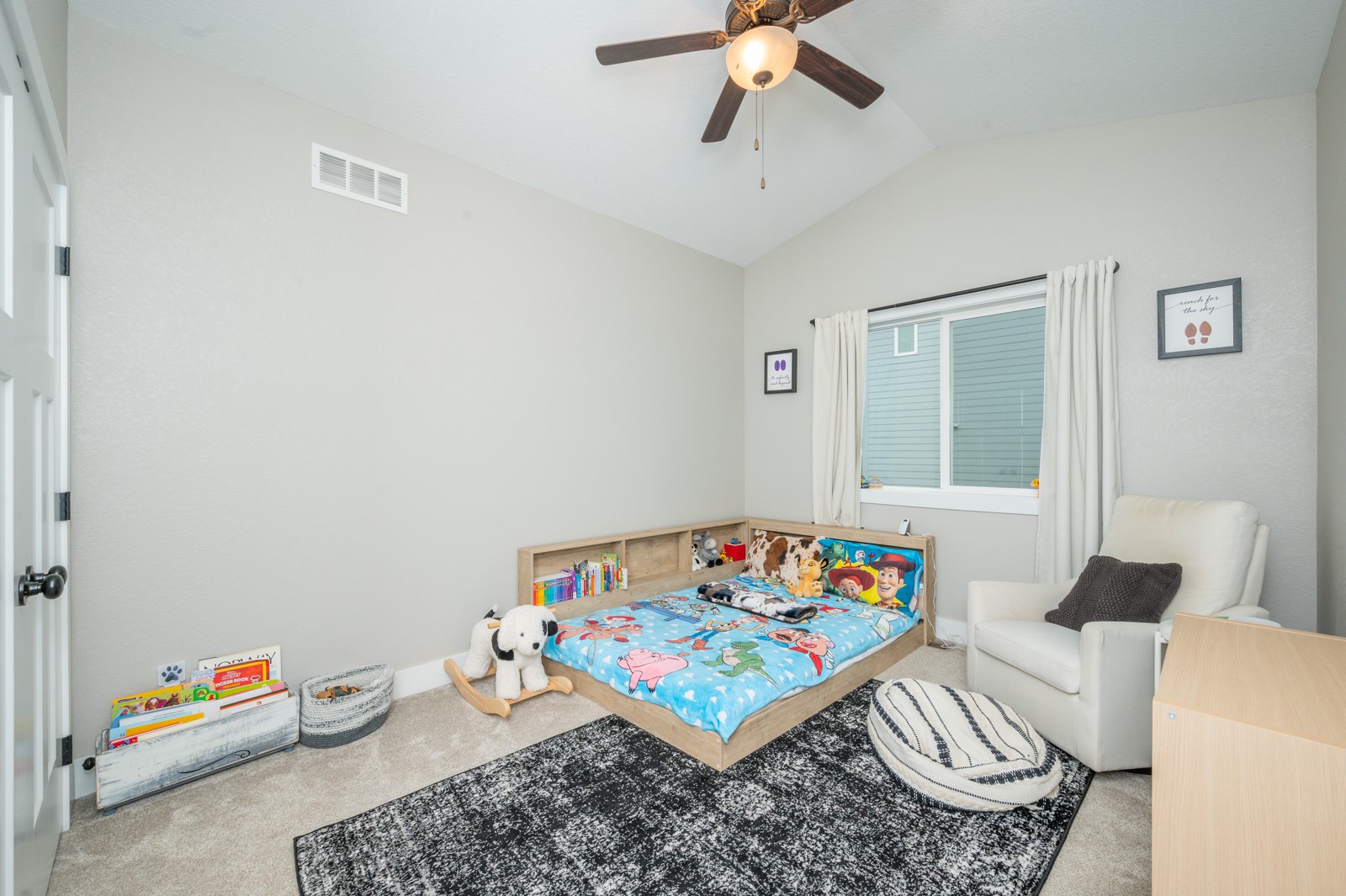 Child's bedroom with colorful cartoon bedding, a low wooden bed, and a white armchair.