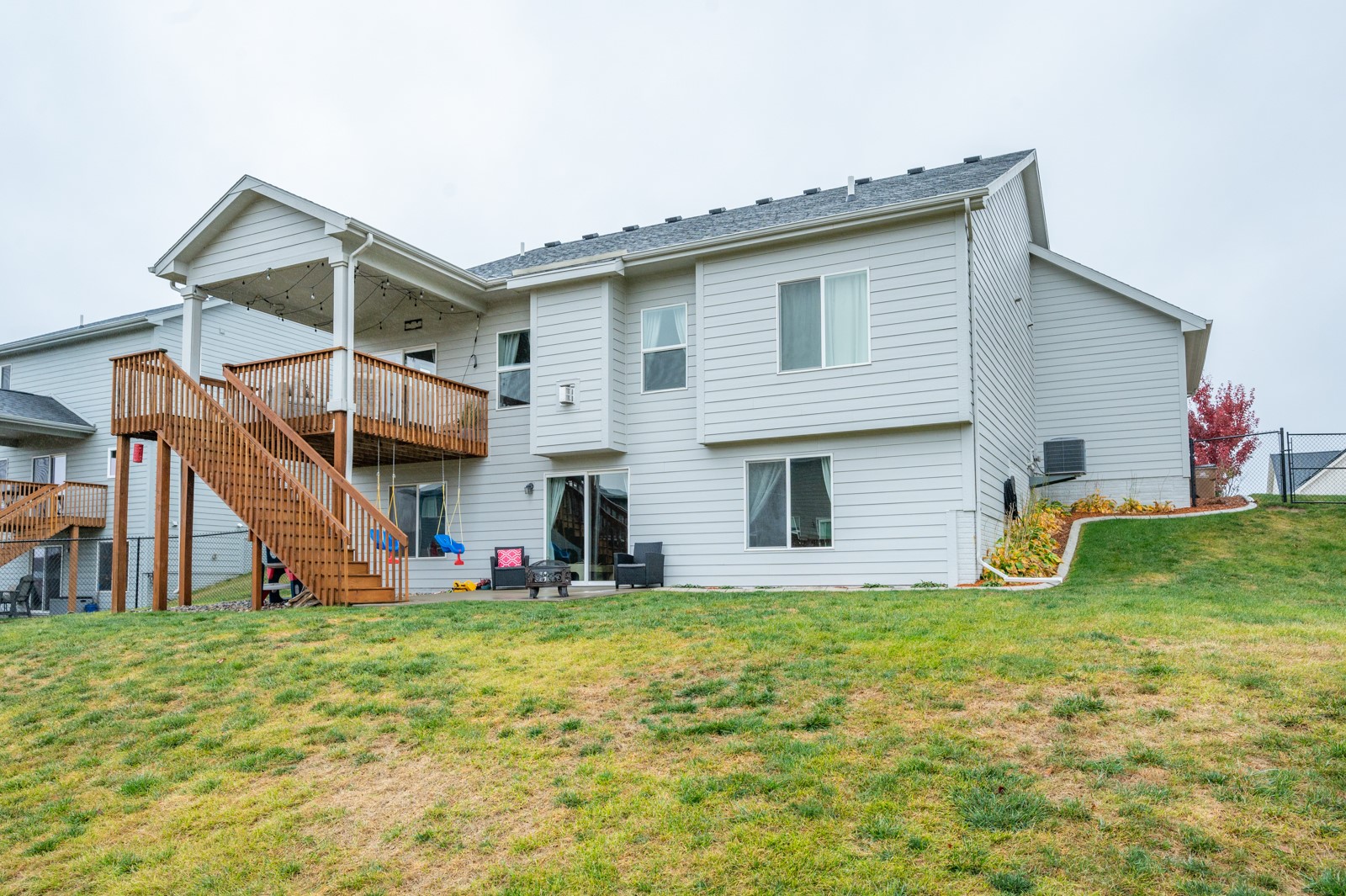 Rear of a two-story gray house with a raised wooden deck, covered patio, and sloping lawn.