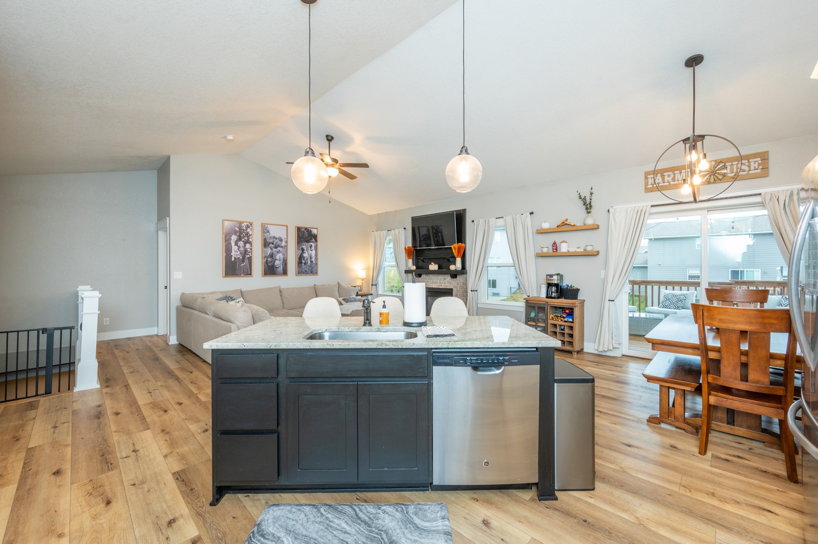 Open-plan kitchen and living area with a dark island, wood floors, fireplace, and deck access.