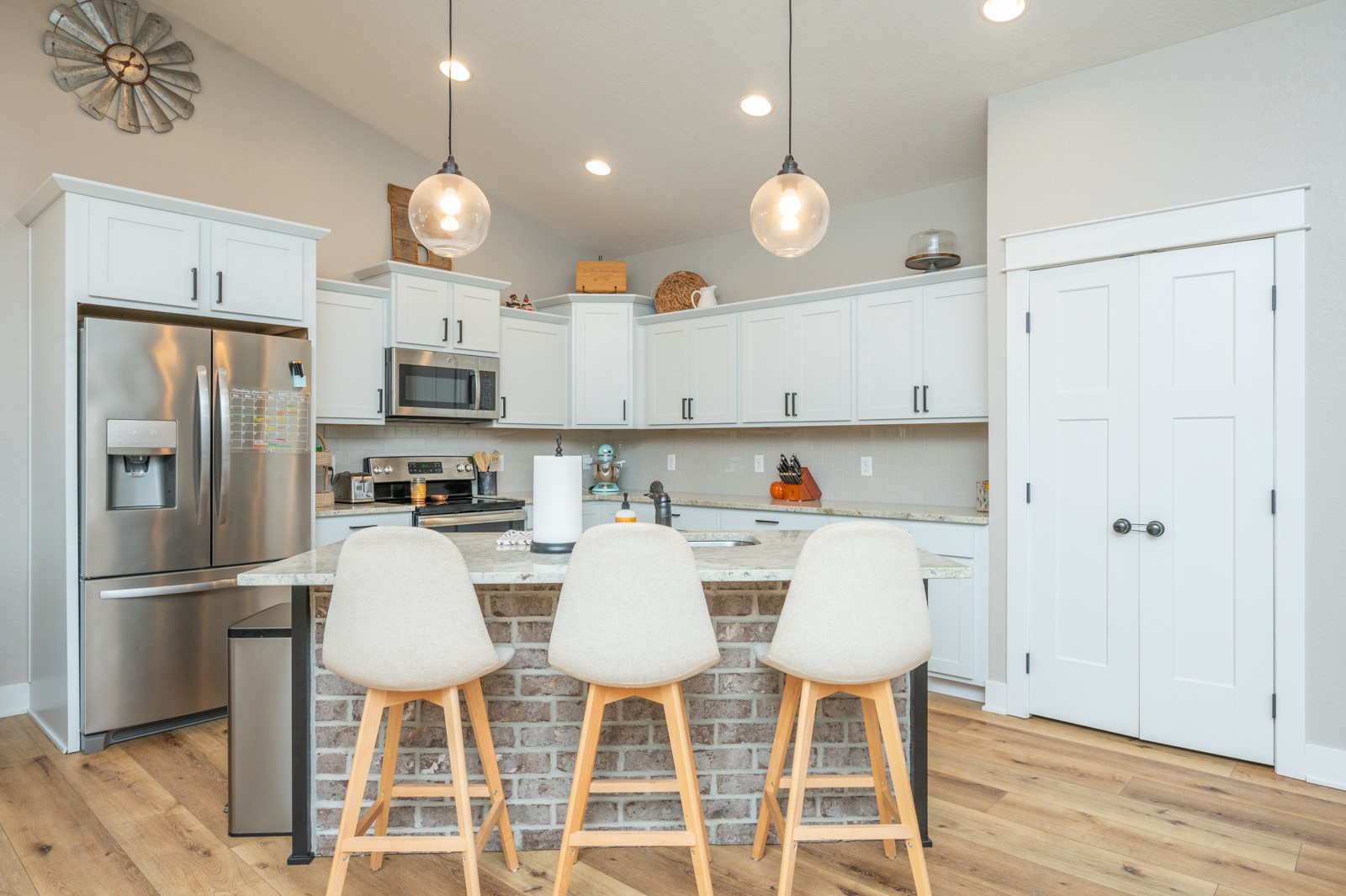Kitchen with white cabinets, stainless appliances, and a brick-front island with three bar stools.