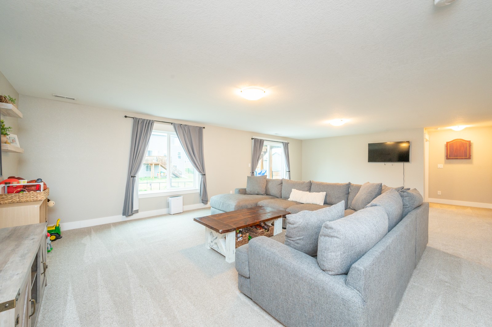Living room with a large gray sectional, wooden coffee table, and two curtained windows.